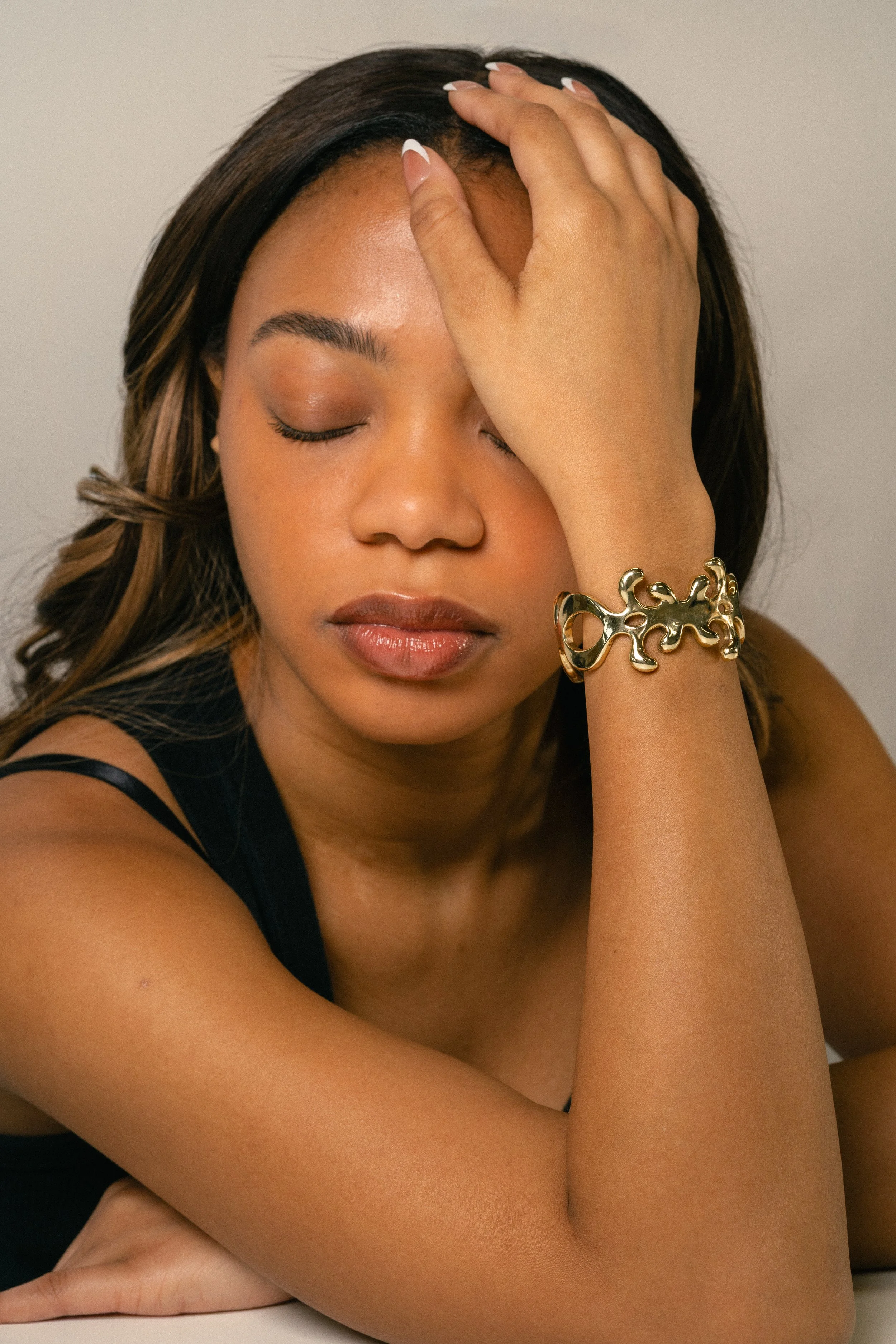 A woman with long hair and a gold bracelet, resting her head on her hand with eyes closed.