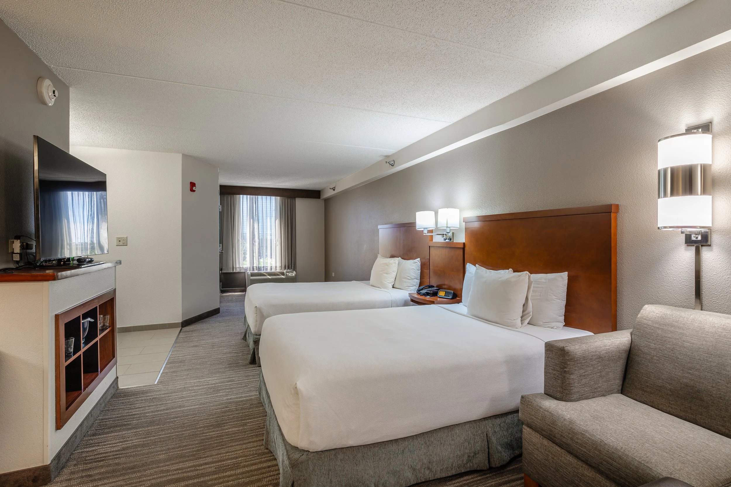 Hotel room with two beds, nightstand, TV, sofa, and window with curtains.