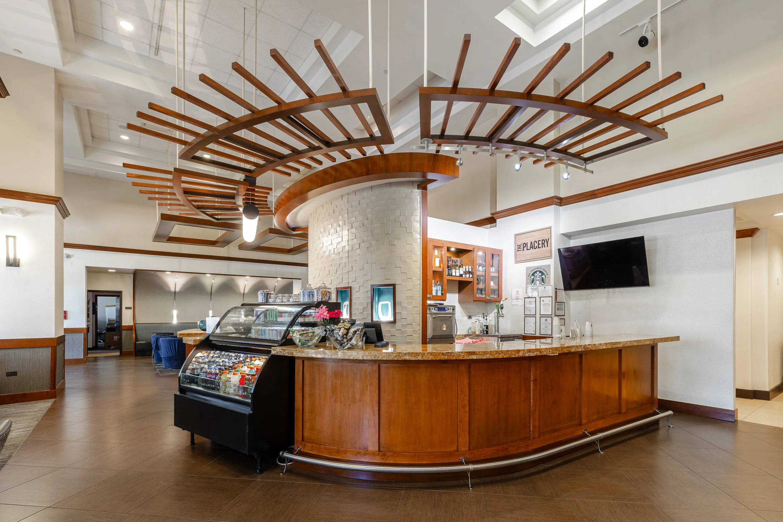Interior of a cafe or restaurant with a curved wooden counter, refrigerated display case, and decorative ceiling wood beams.
