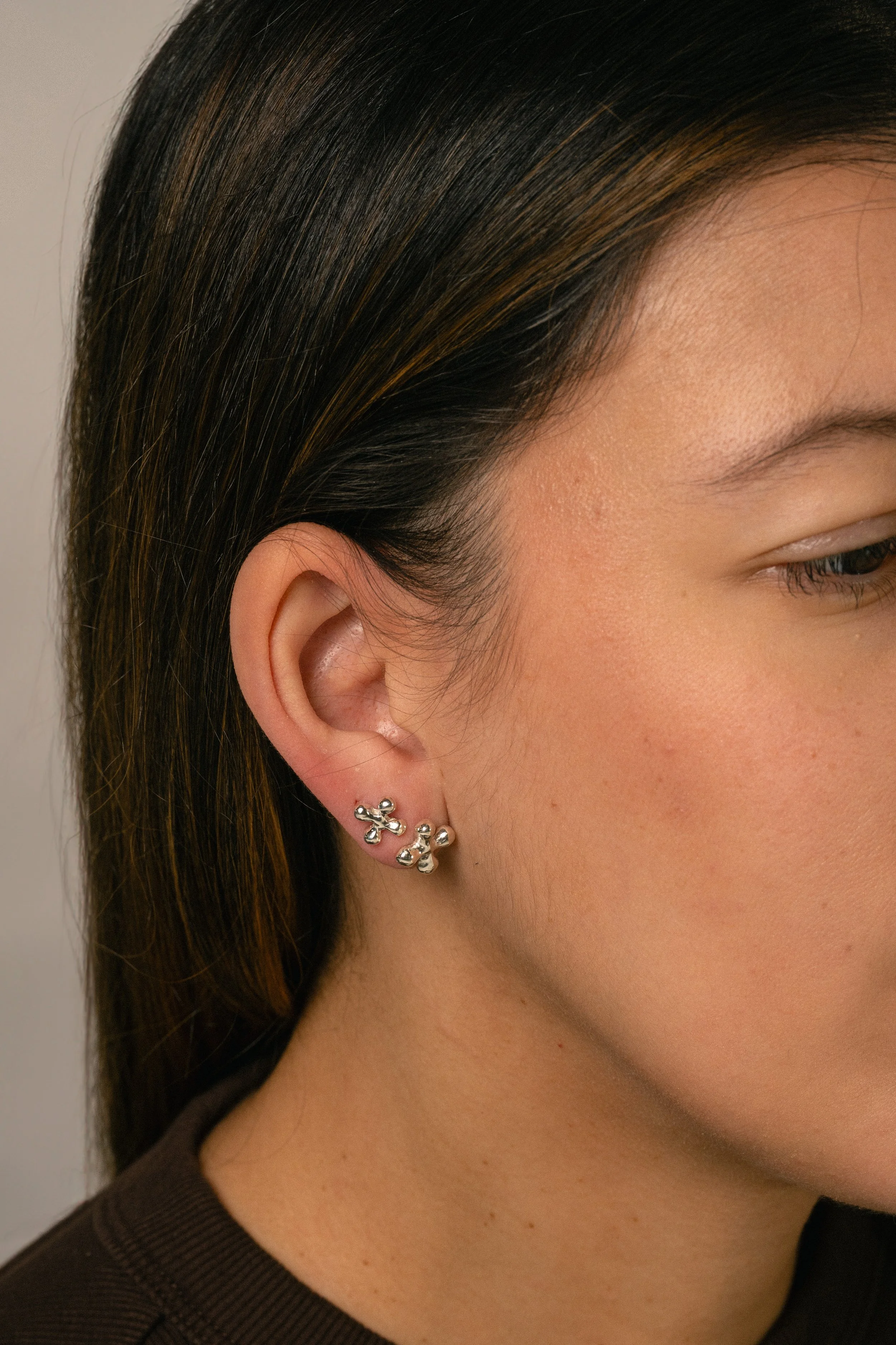 Close-up of a woman's right ear wearing a silver earring with a floral design. She has dark brown hair with subtle highlights and is wearing a dark brown top.