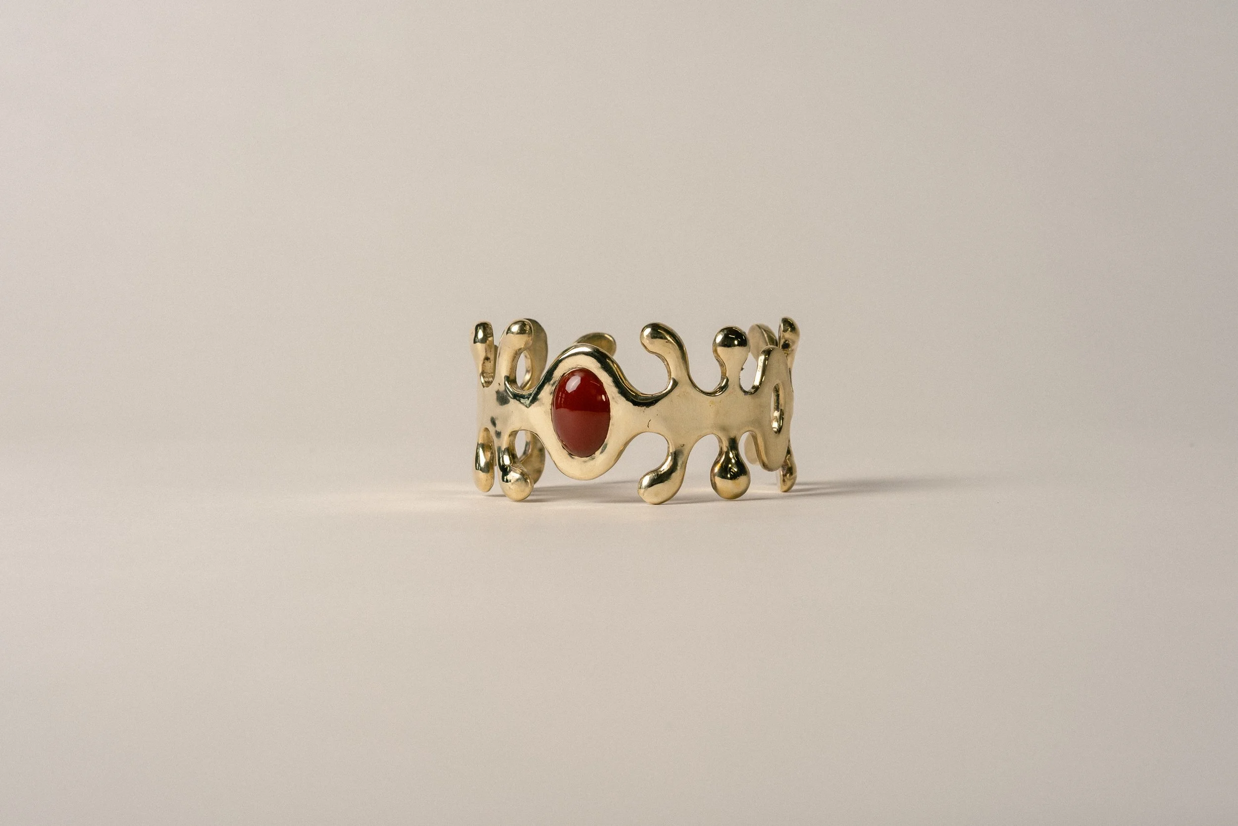 Gold ring with an intricate openwork design and a red oval gemstone in the center placed on a plain white background.