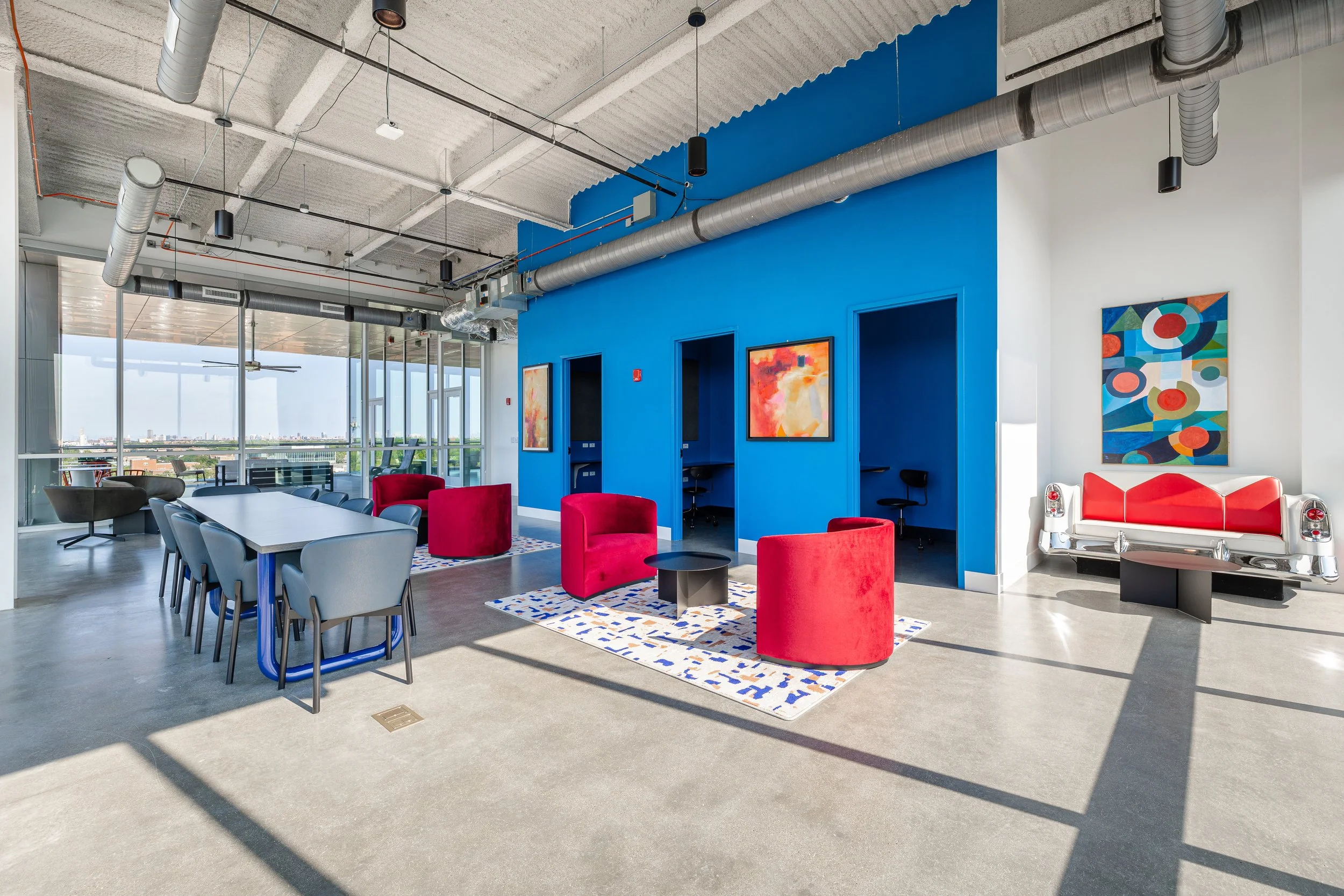 Modern rooftop lounge with colorful chairs, artwork, and city views.