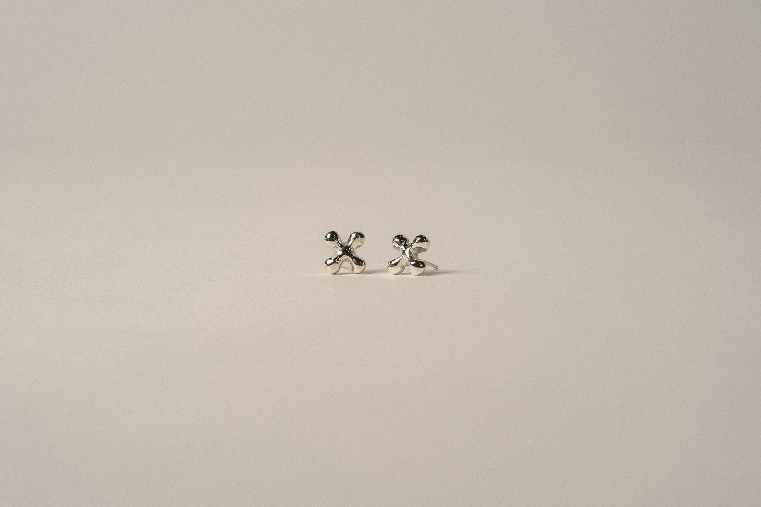 Small silver earrings with a flower-shaped design on a plain light background.