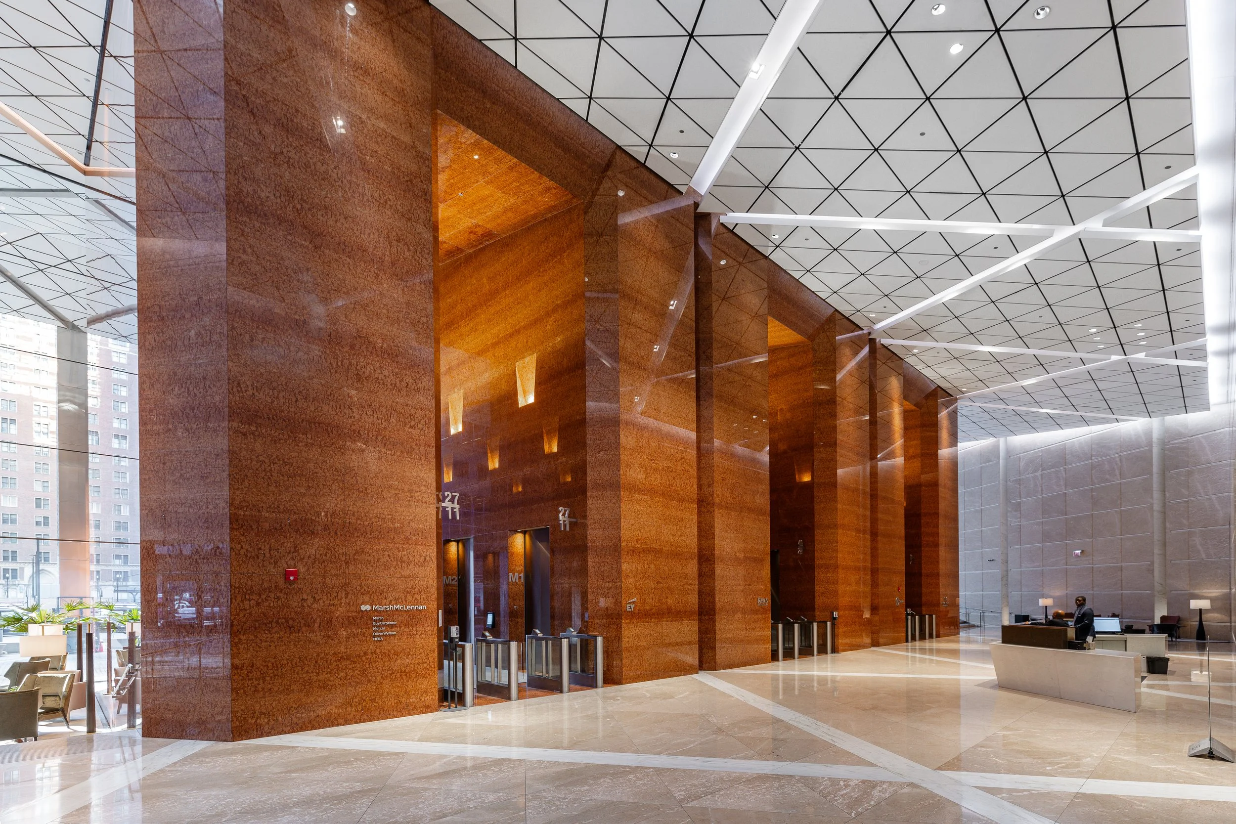 Interior view of a modern office lobby with high ceilings, large marble columns, and elevator banks.