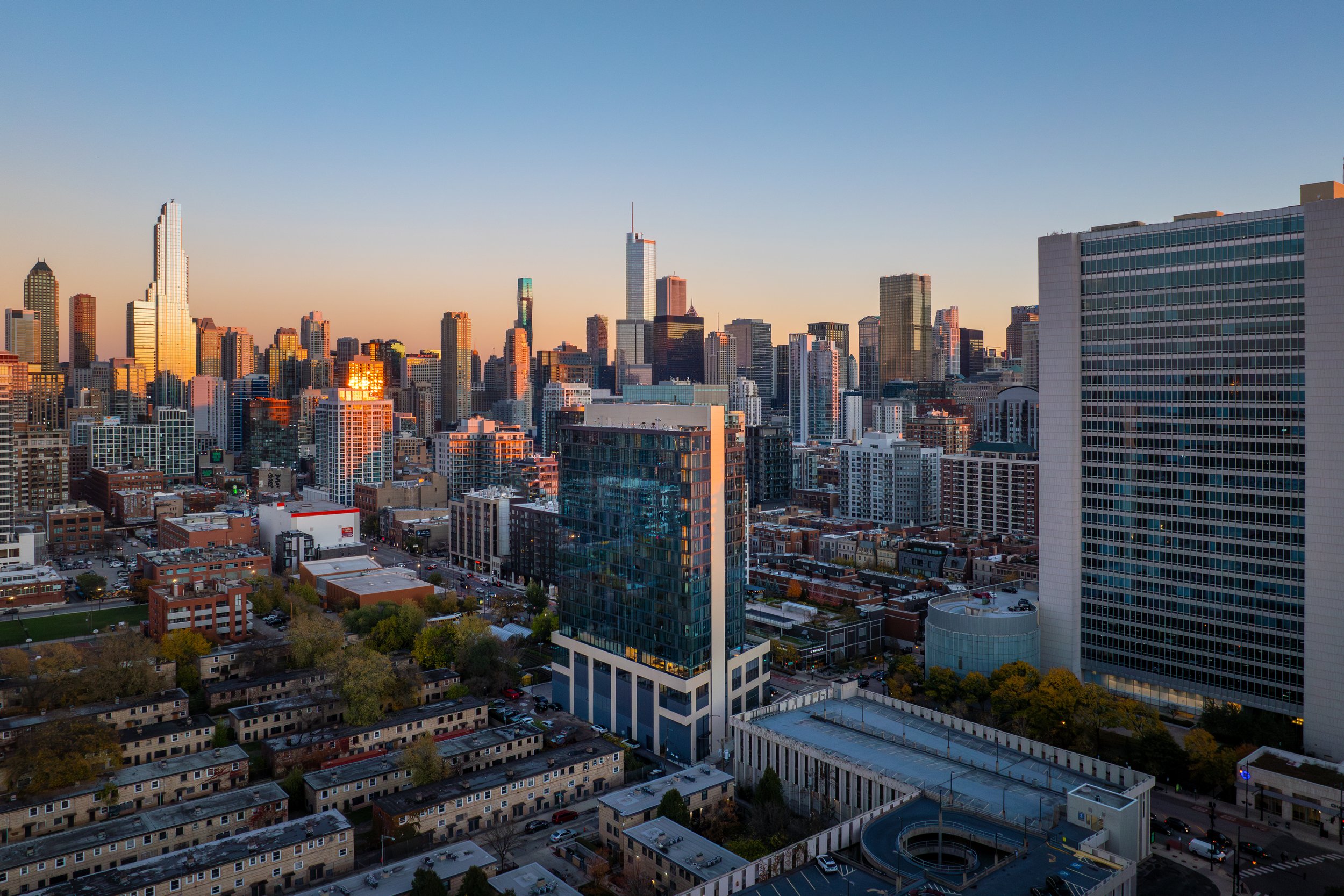 City skyline at sunset with tall skyscrapers and mid-rise buildings in downtown area, view of a modern glass building in foreground, clear sky