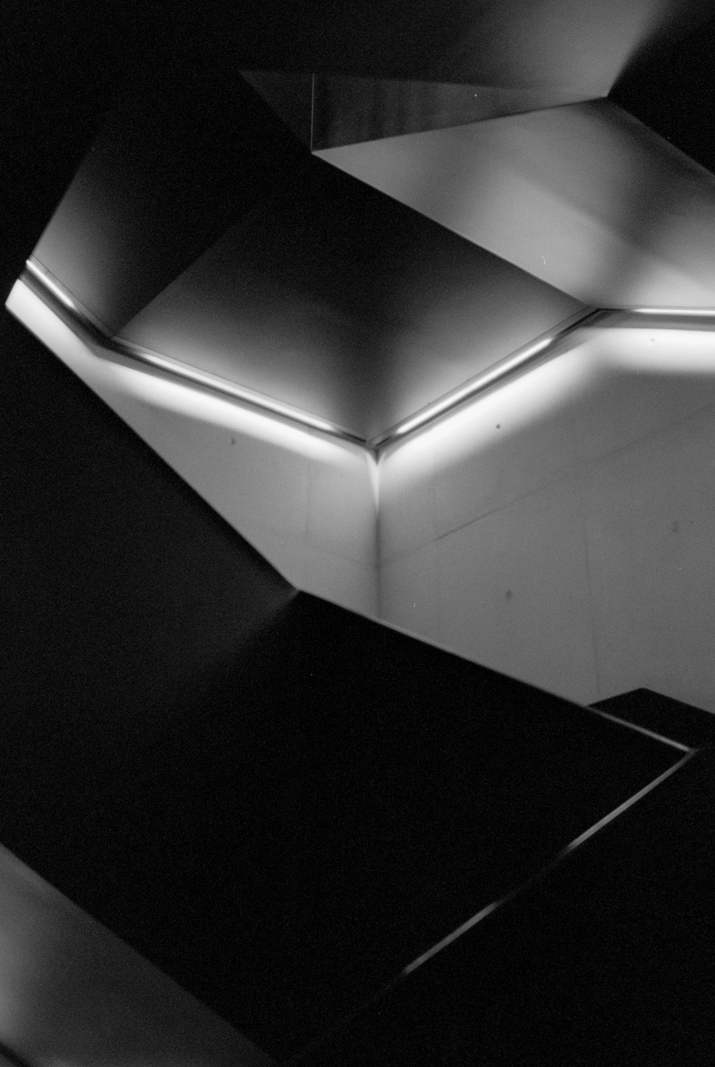 Close-up of a modern ceiling with curved and straight lines, illuminated by strip lighting.