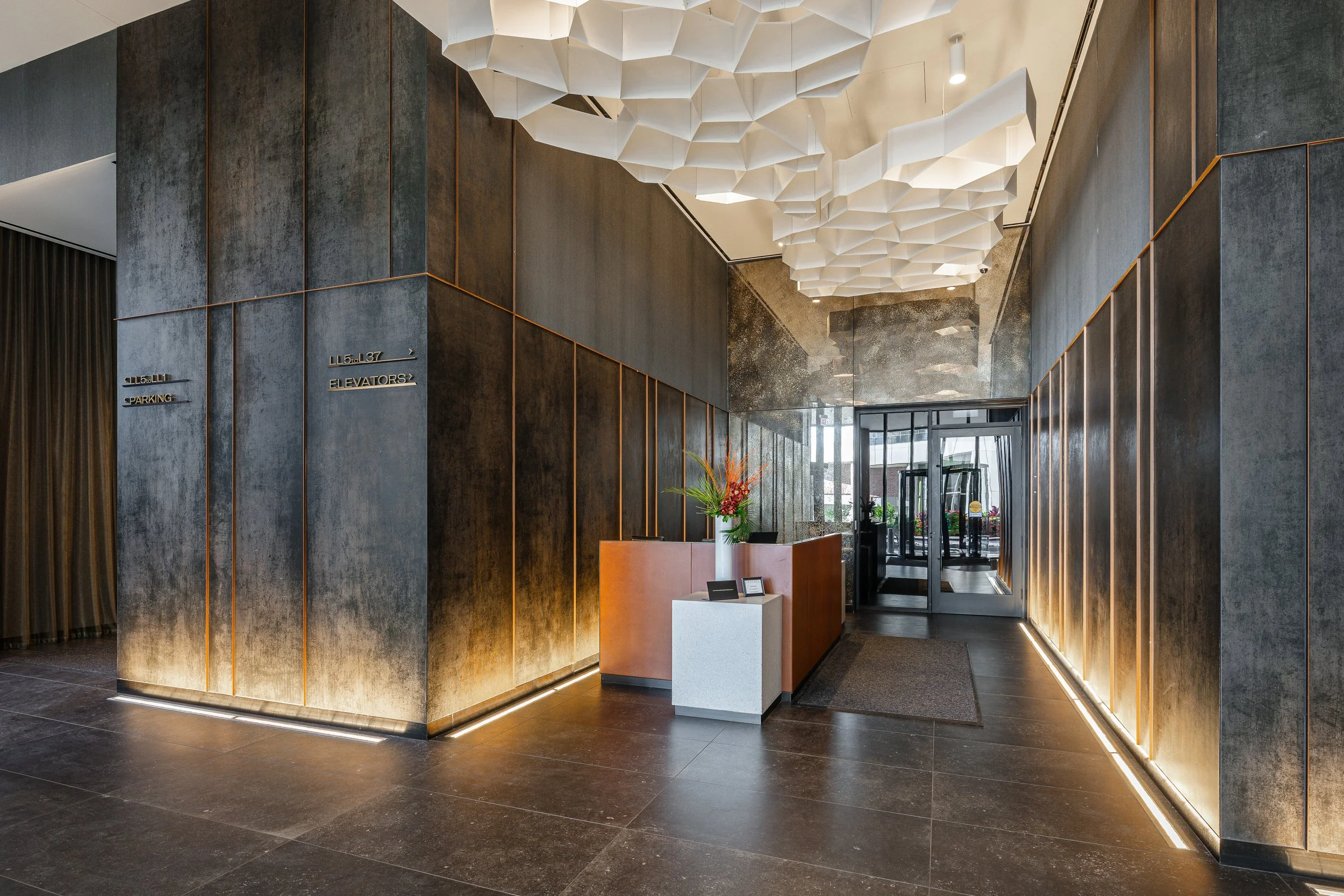 Modern hotel lobby with dark textured walls, a reception counter with a flower arrangement, and stylish lighting fixtures on the ceiling.