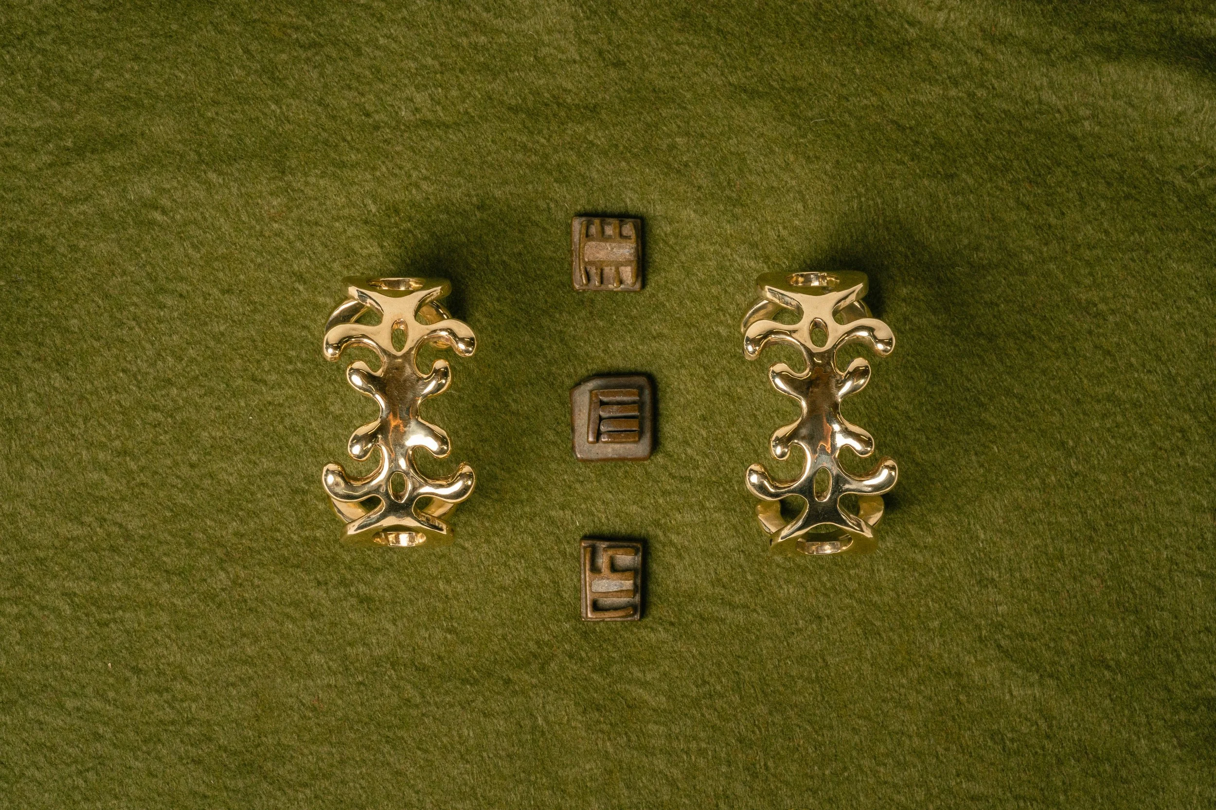 Two gold ornate hinges and three small black metal fasteners on green fabric background.