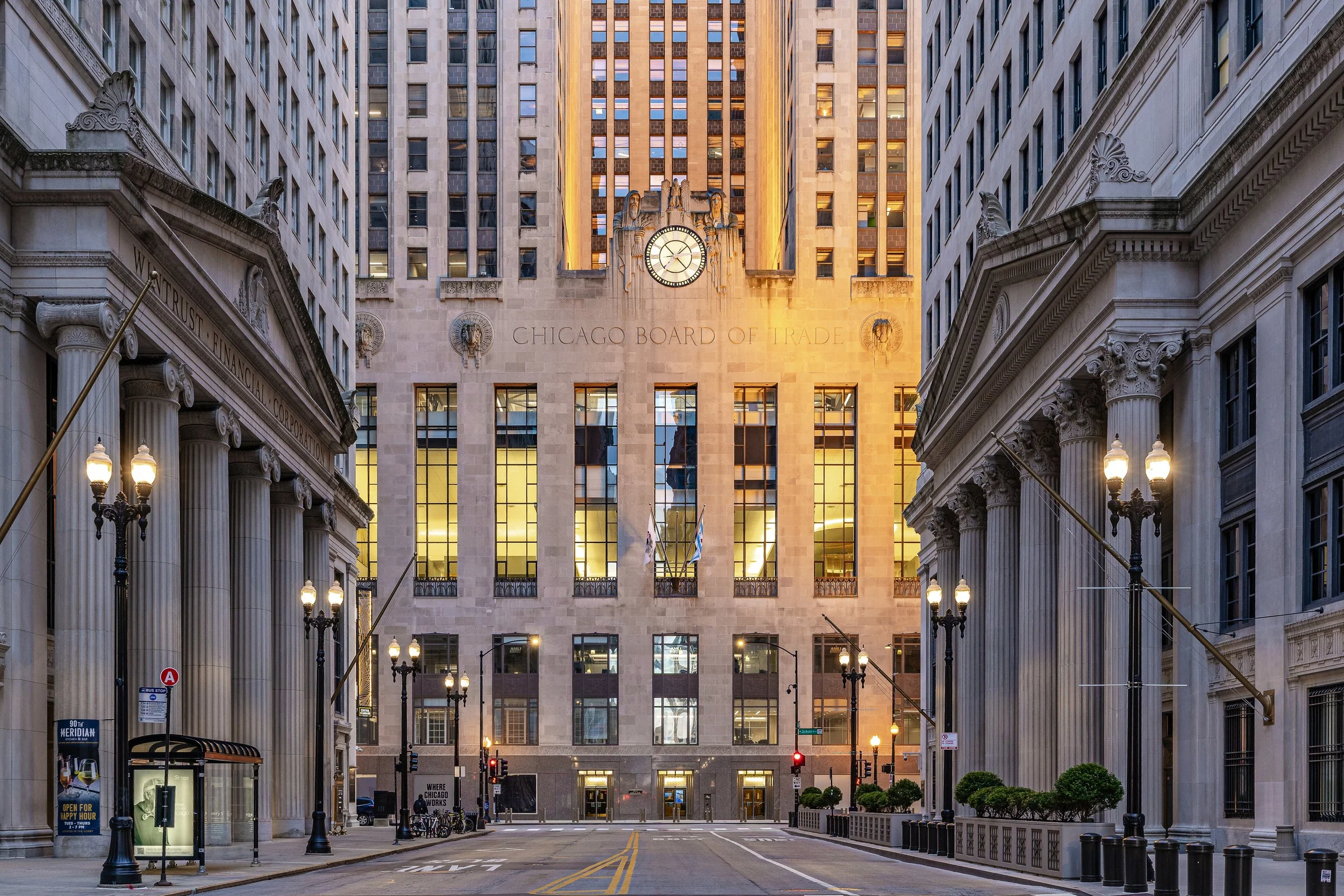 Empty street in front of Chicago Board of Trade building with classical architectural style and surrounding tall buildings, early morning or late evening lighting.