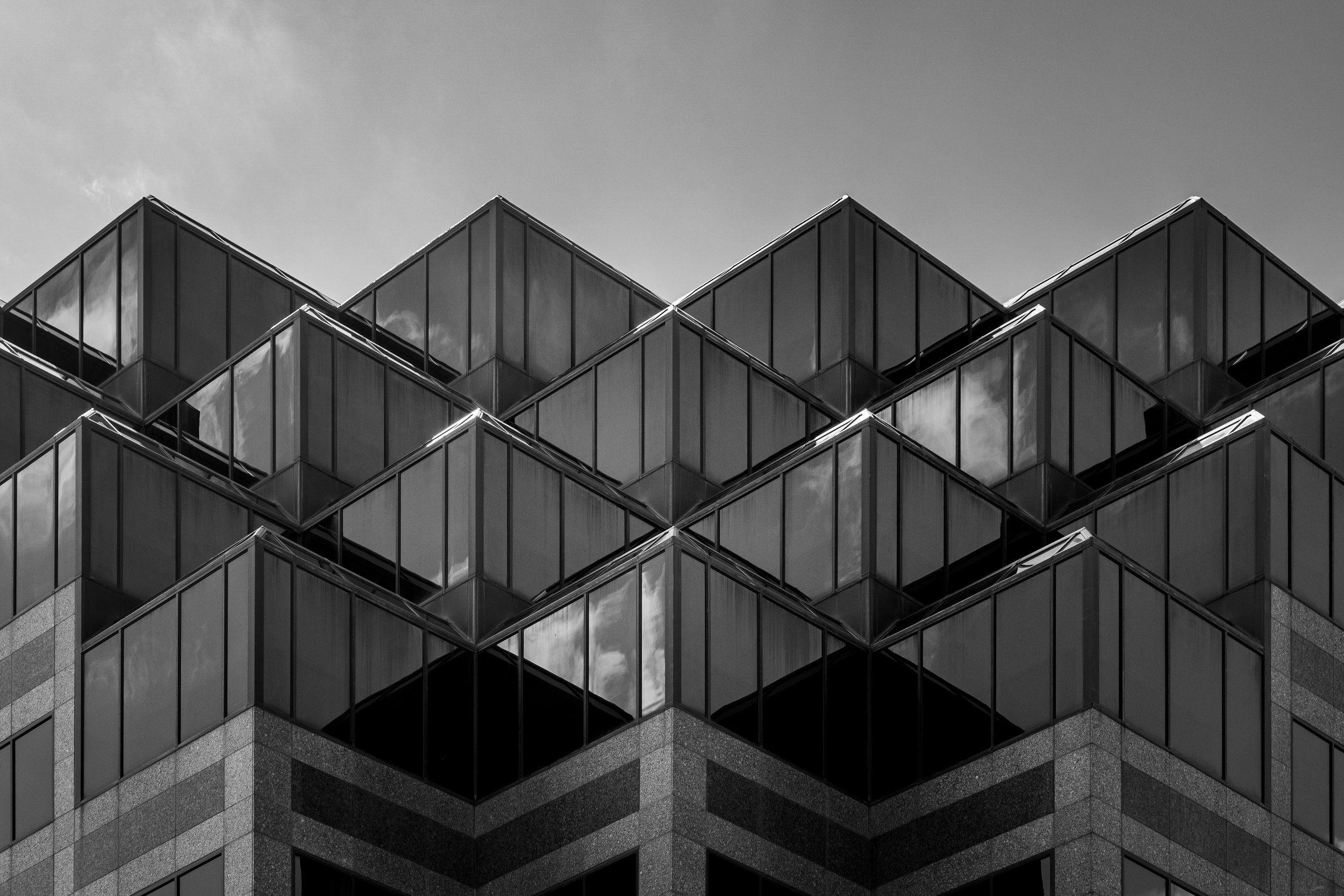 Black and white photograph of the corner of a modern office building with reflective glass windows arranged in a geometric, stepped pattern.