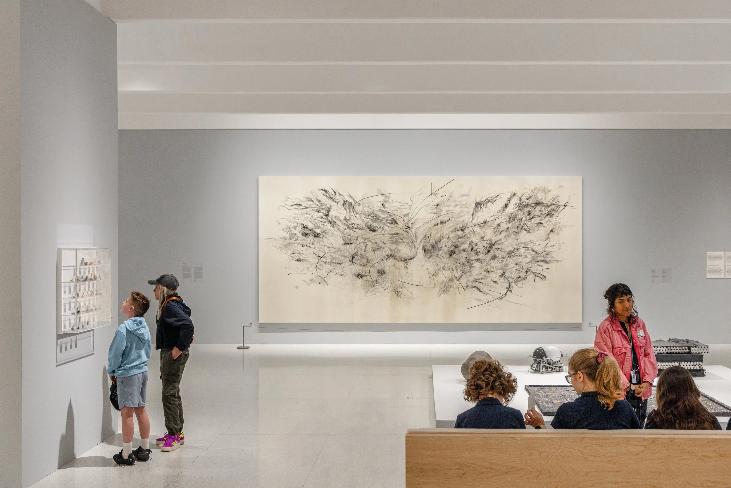 People viewing artwork and displays in a modern art museum with white walls and a large abstract black-and-white painting.