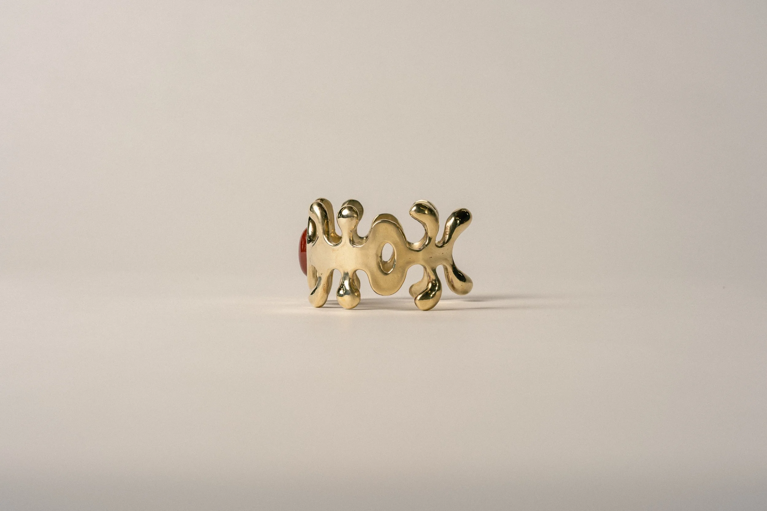A gold ring with an abstract, irregular design, placed against a plain, light-colored background.