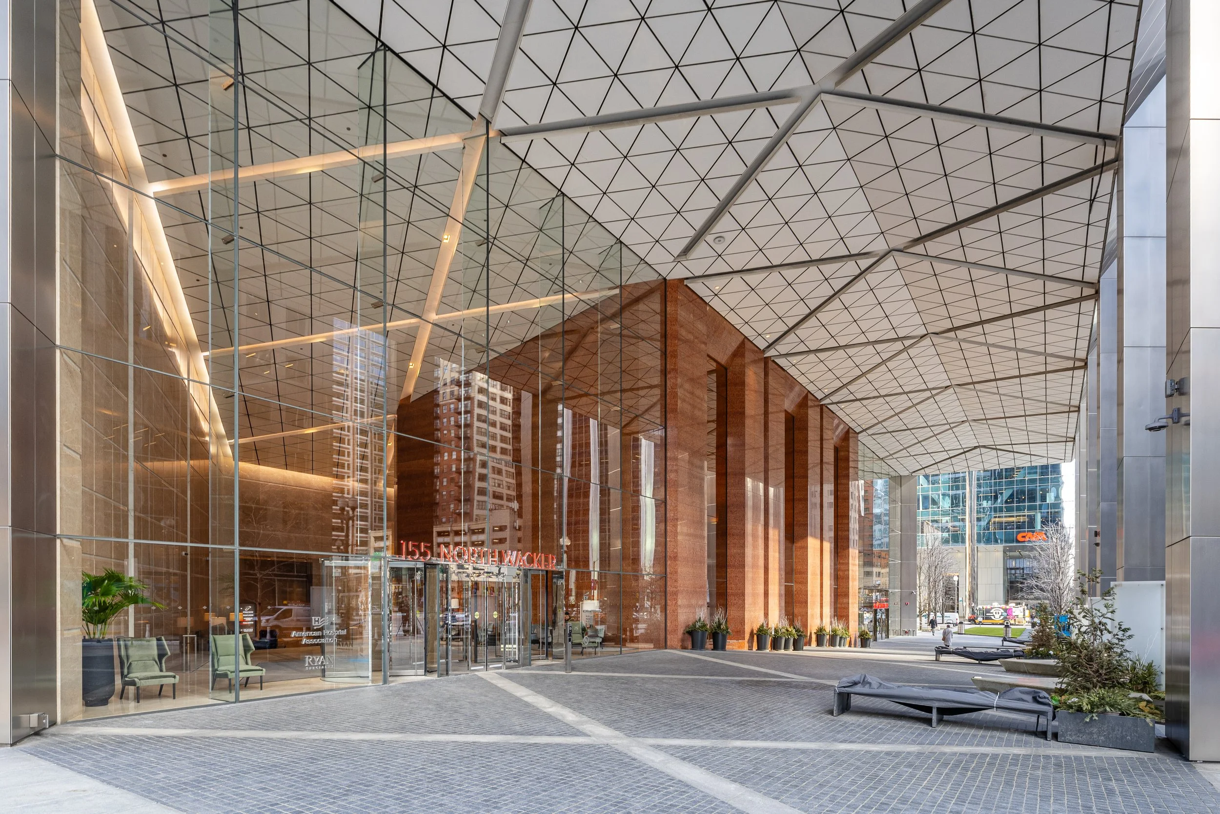 Modern building's entrance with glass facade, brick columns, and a distinctive geometric roof canopy
