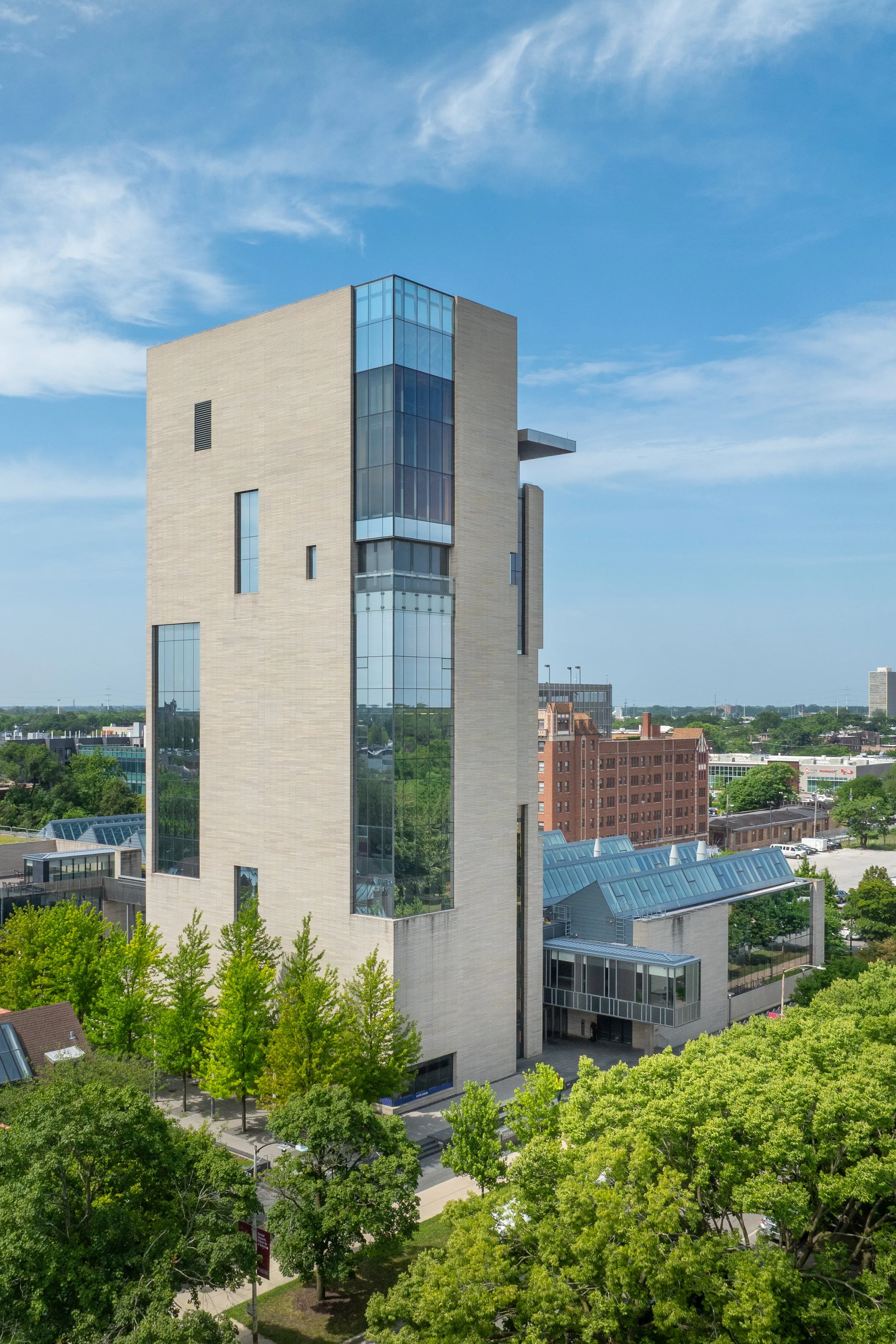 Modern high-rise building with reflective glass windows amidst greenery with a bright blue sky.