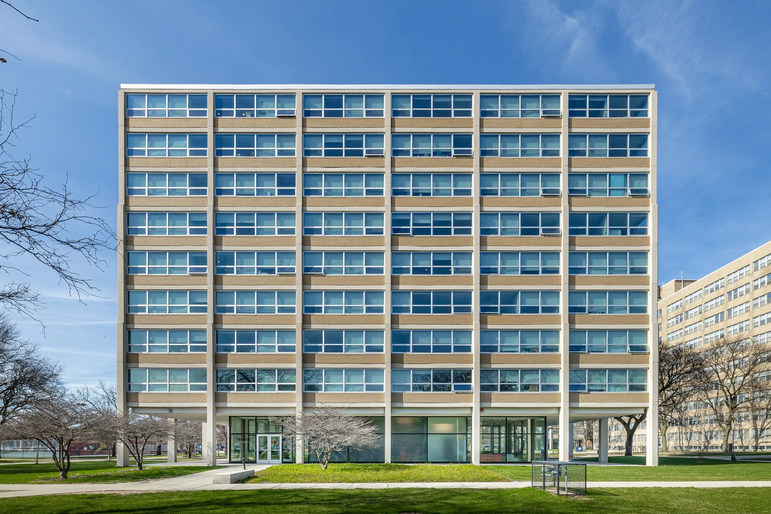 A modern multi-story office building with glass windows and a landscaped front yard, under a blue sky.