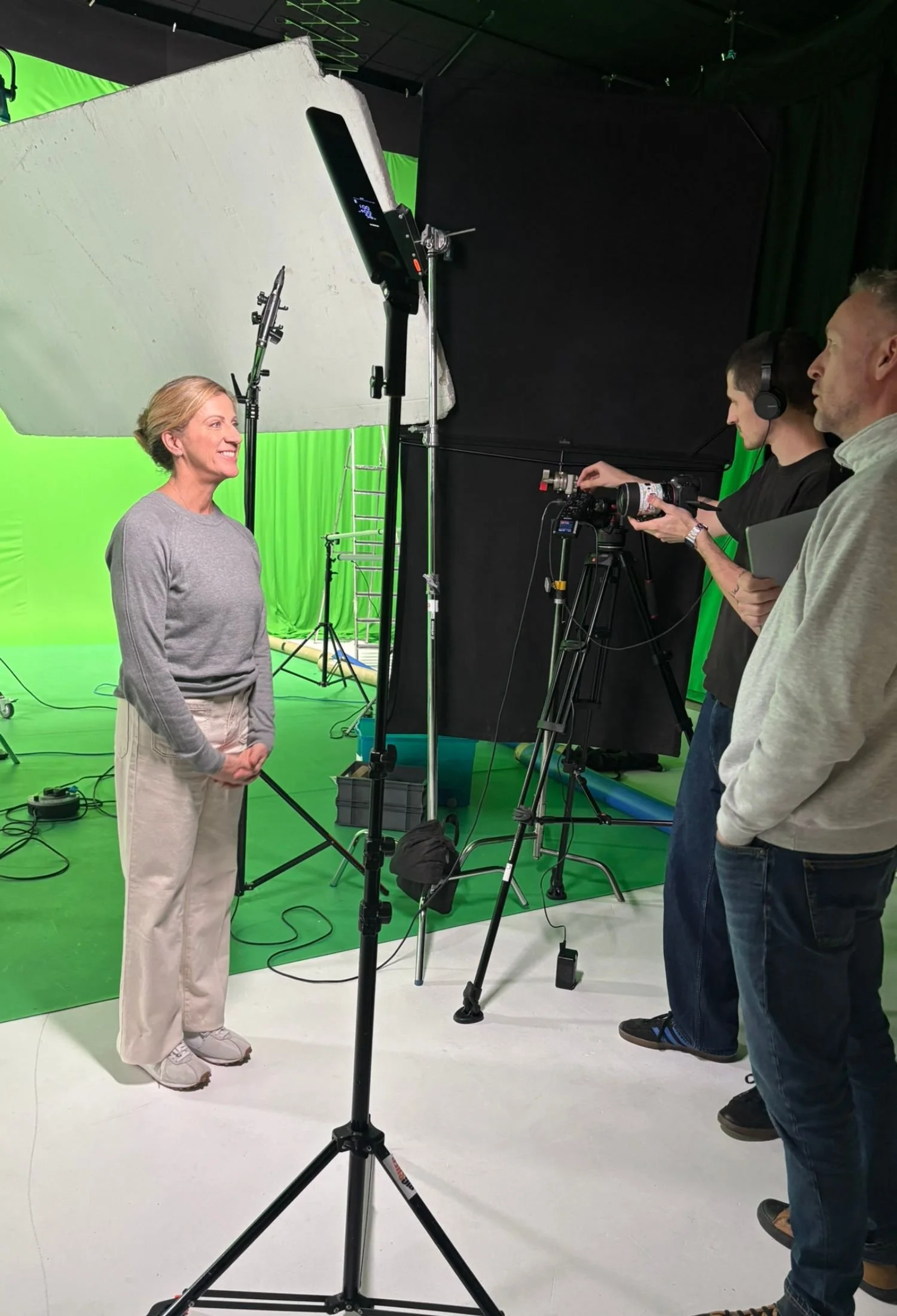is standing in front of green screen and studio lighting on a film set.
