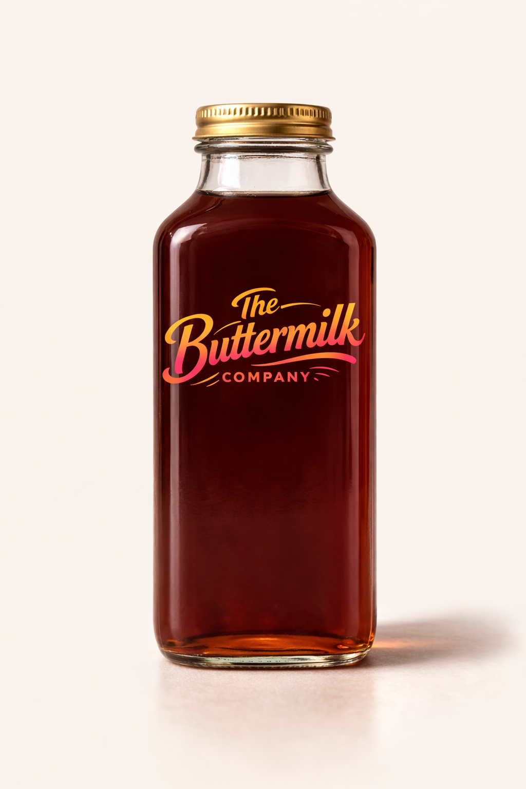 A glass jar with a golden lid, filled with dark red liquid, labeled 'The Buttermilk Company' in orange and pink script.