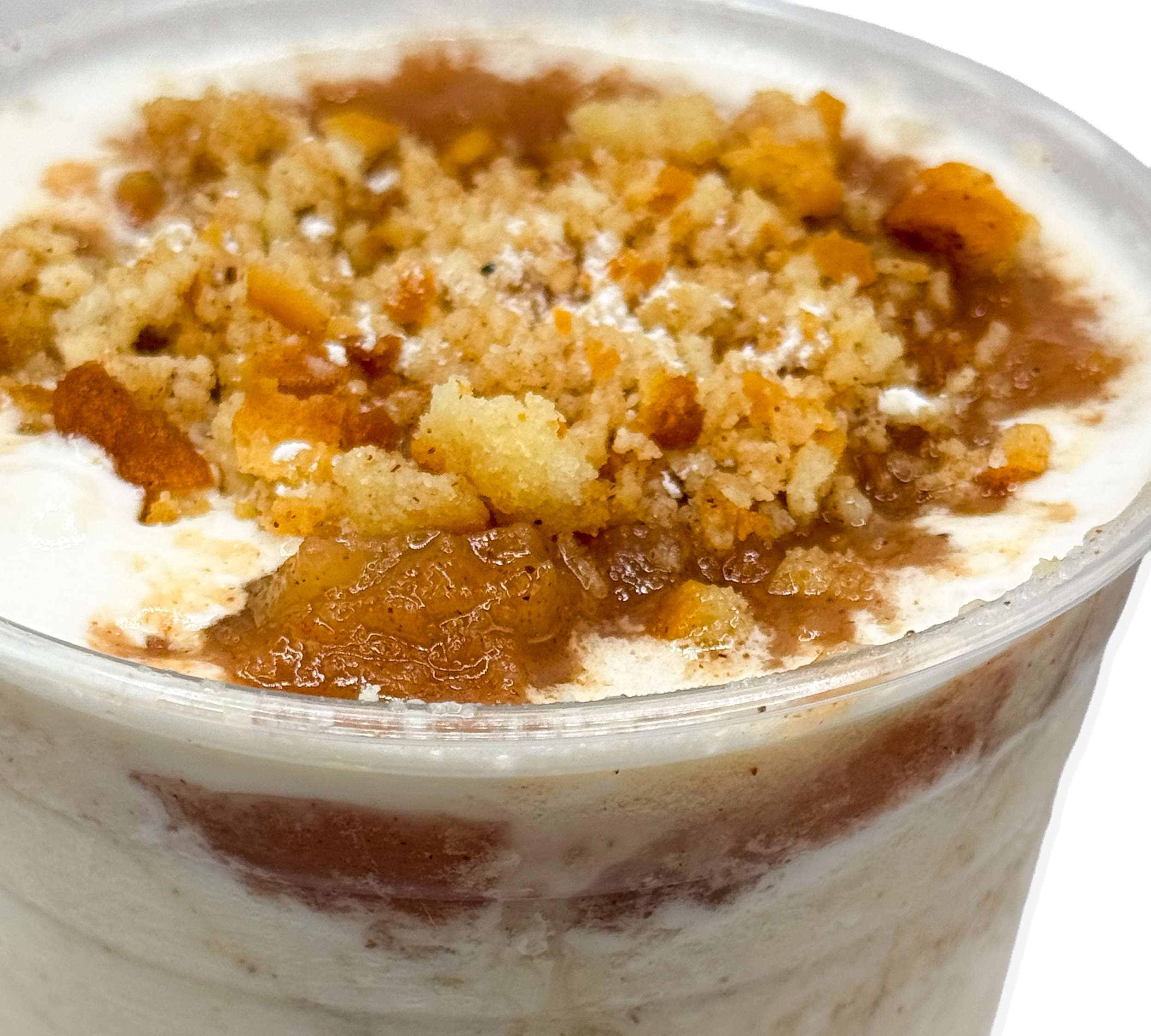 Close-up of a dessert in a clear cup, topped with crumbly streusel and sauce.