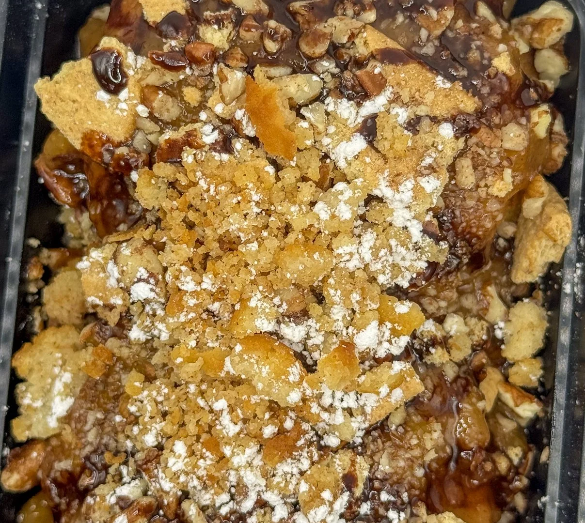 Close-up of a dessert with crushed cookies, chocolate, and powder sprinkled on top.