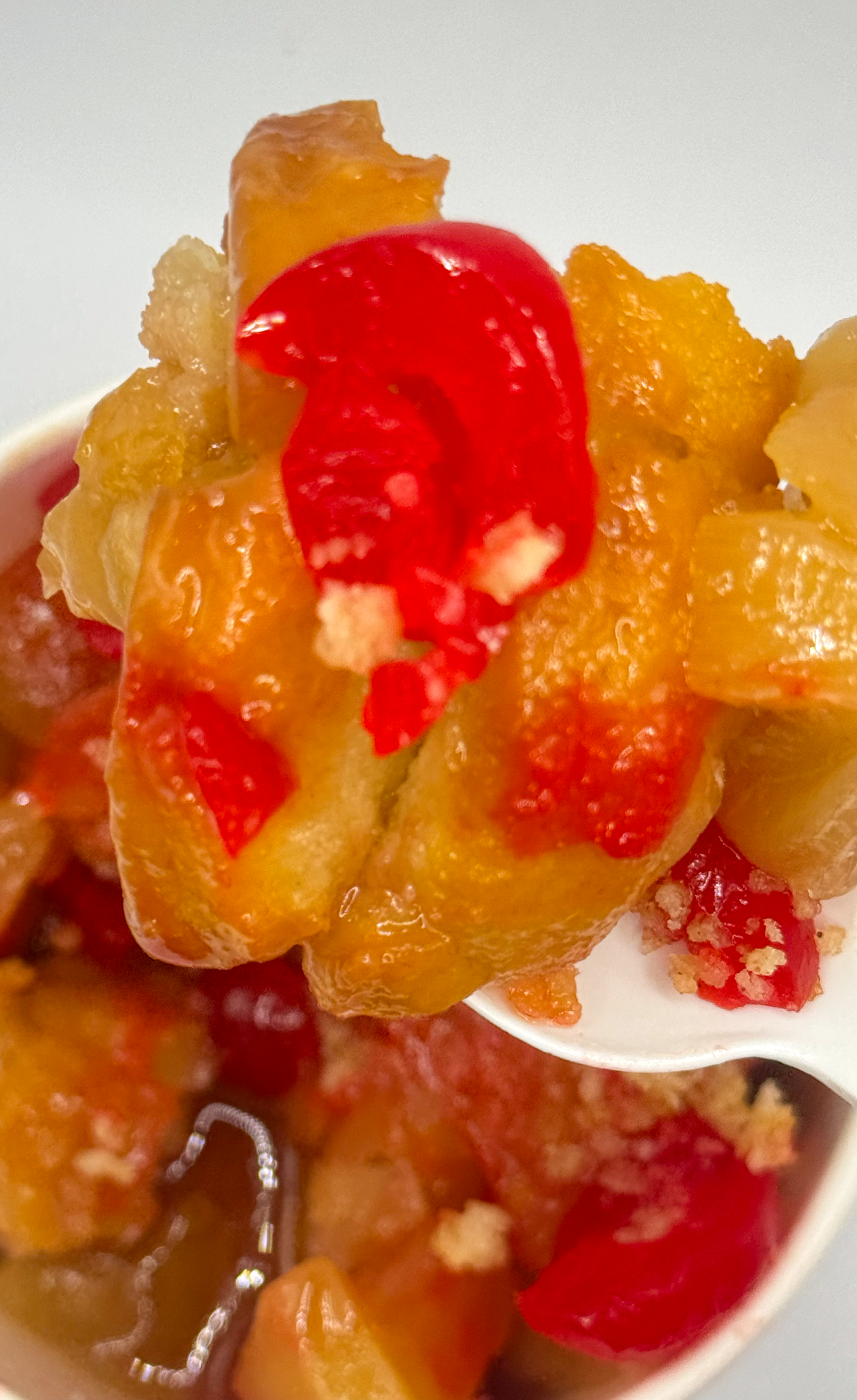 Close-up of a spoonful of pineapple, cherry, and other fruit chunks in a dessert.