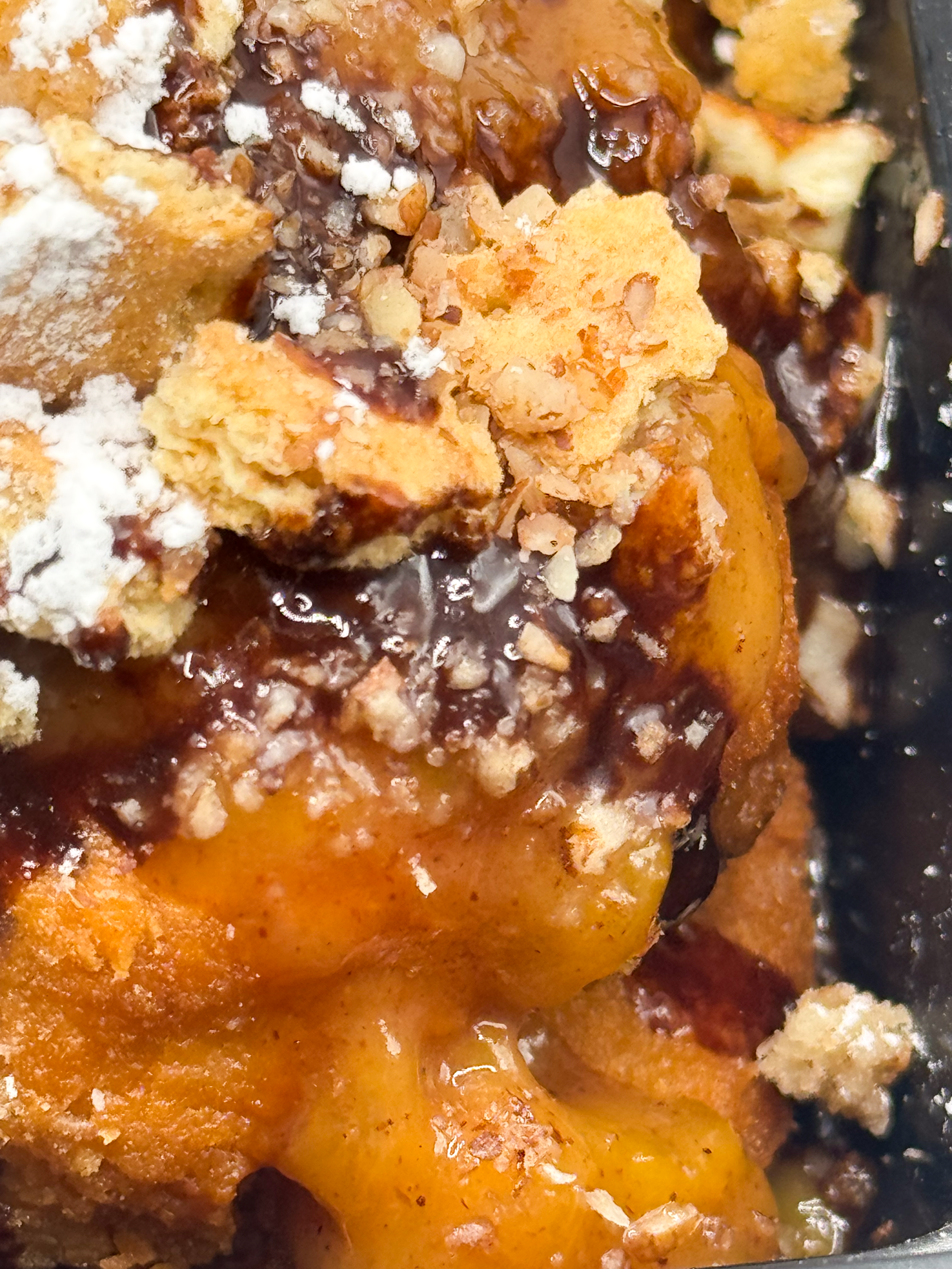 Close-up of a dessert with yellow cake, chocolate sauce, whipped cream, and crumbled cookies or nuts.