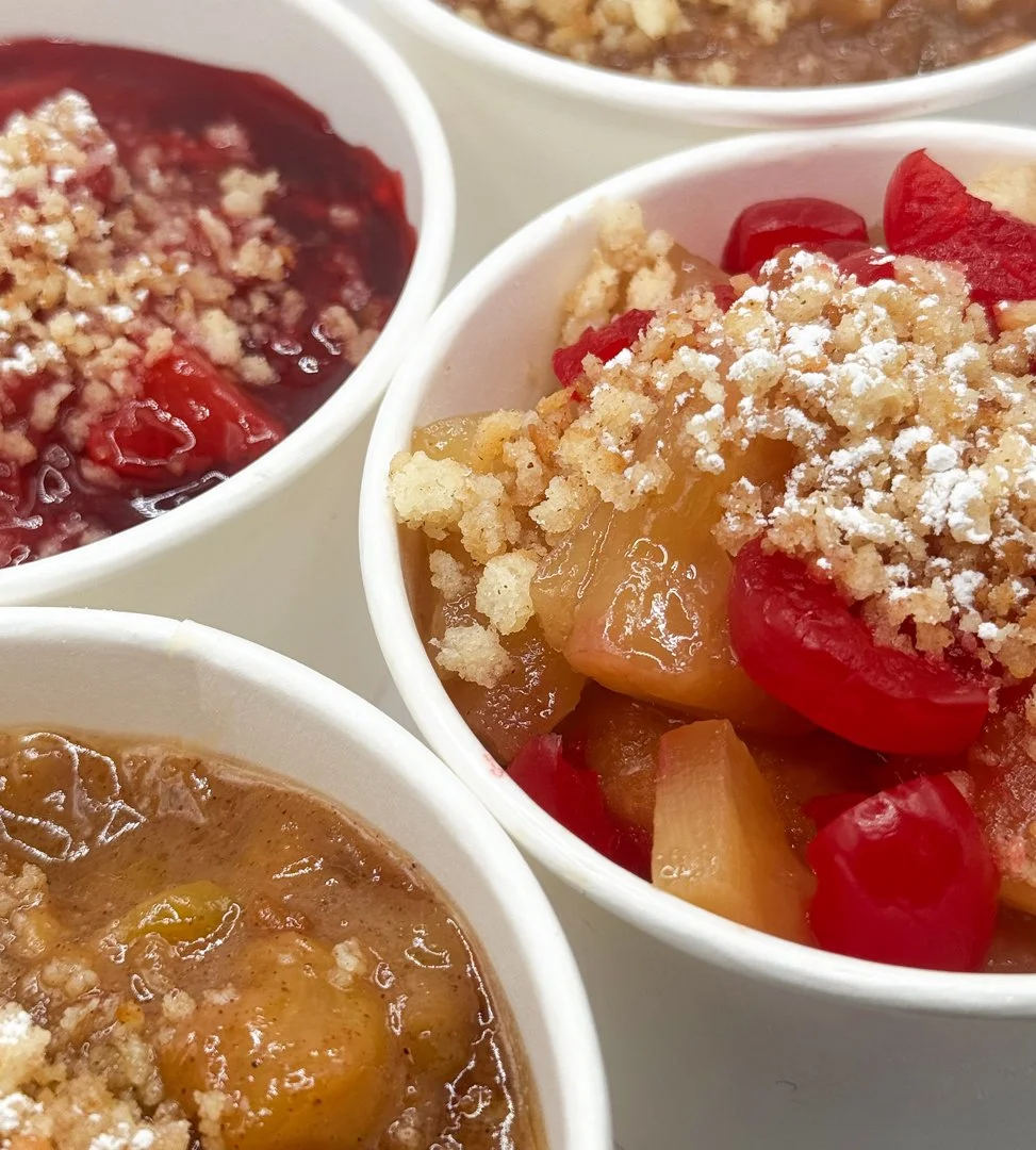 Close-up of three white bowls filled with fruit cobbler topped with crumbly streusel and powdered sugar.