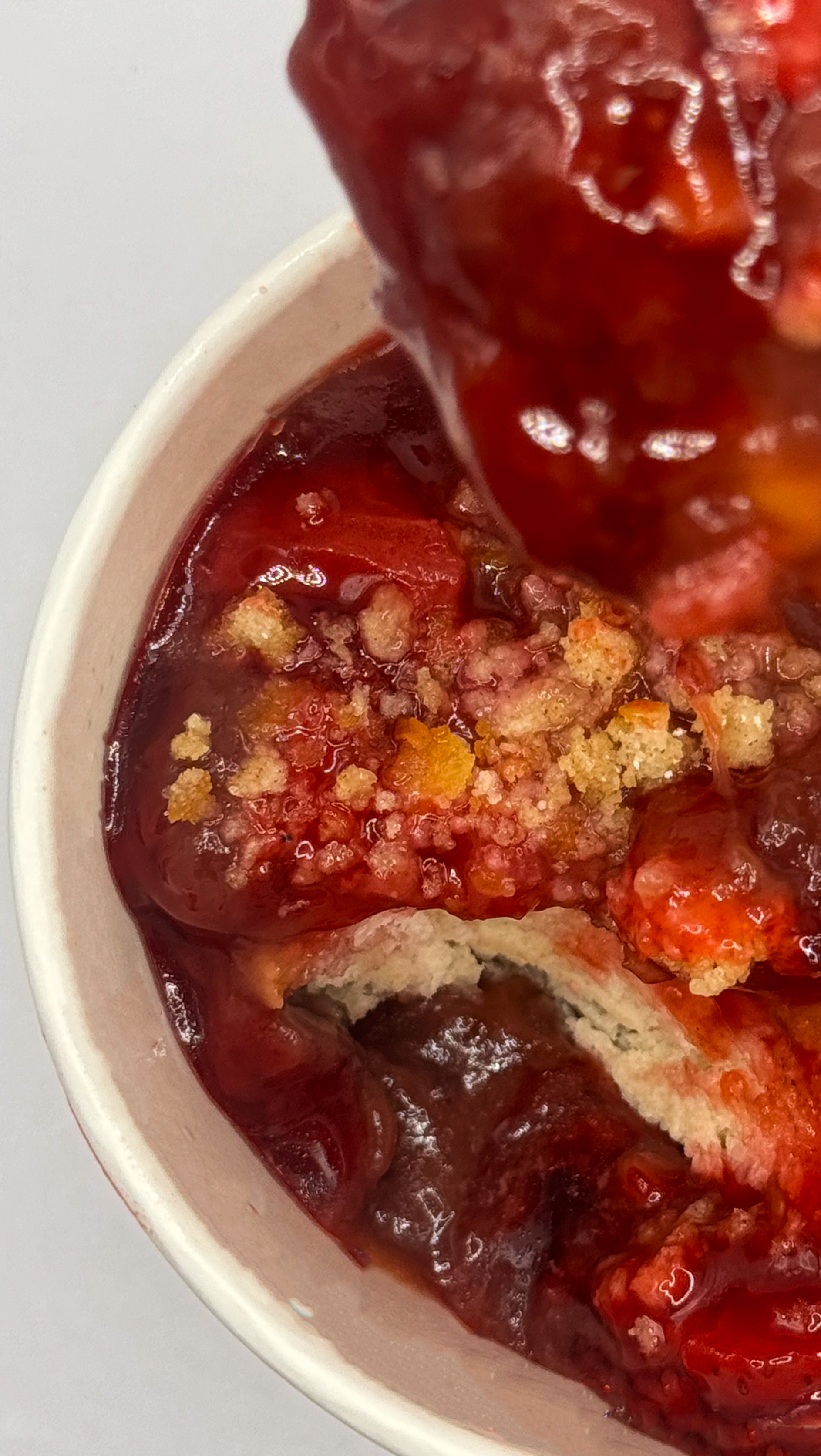 Close-up of a cherry dessert with a crumb topping in a white paper cup.