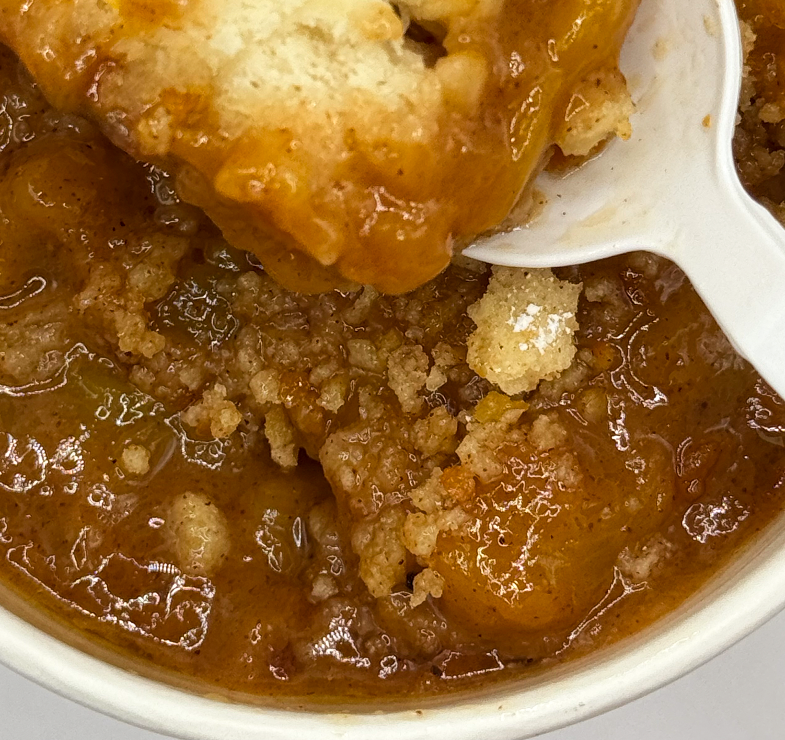 Close-up of a serving spoon with mashed potatoes and beef gravy with ground beef and seasonings in a bowl of beef stew.