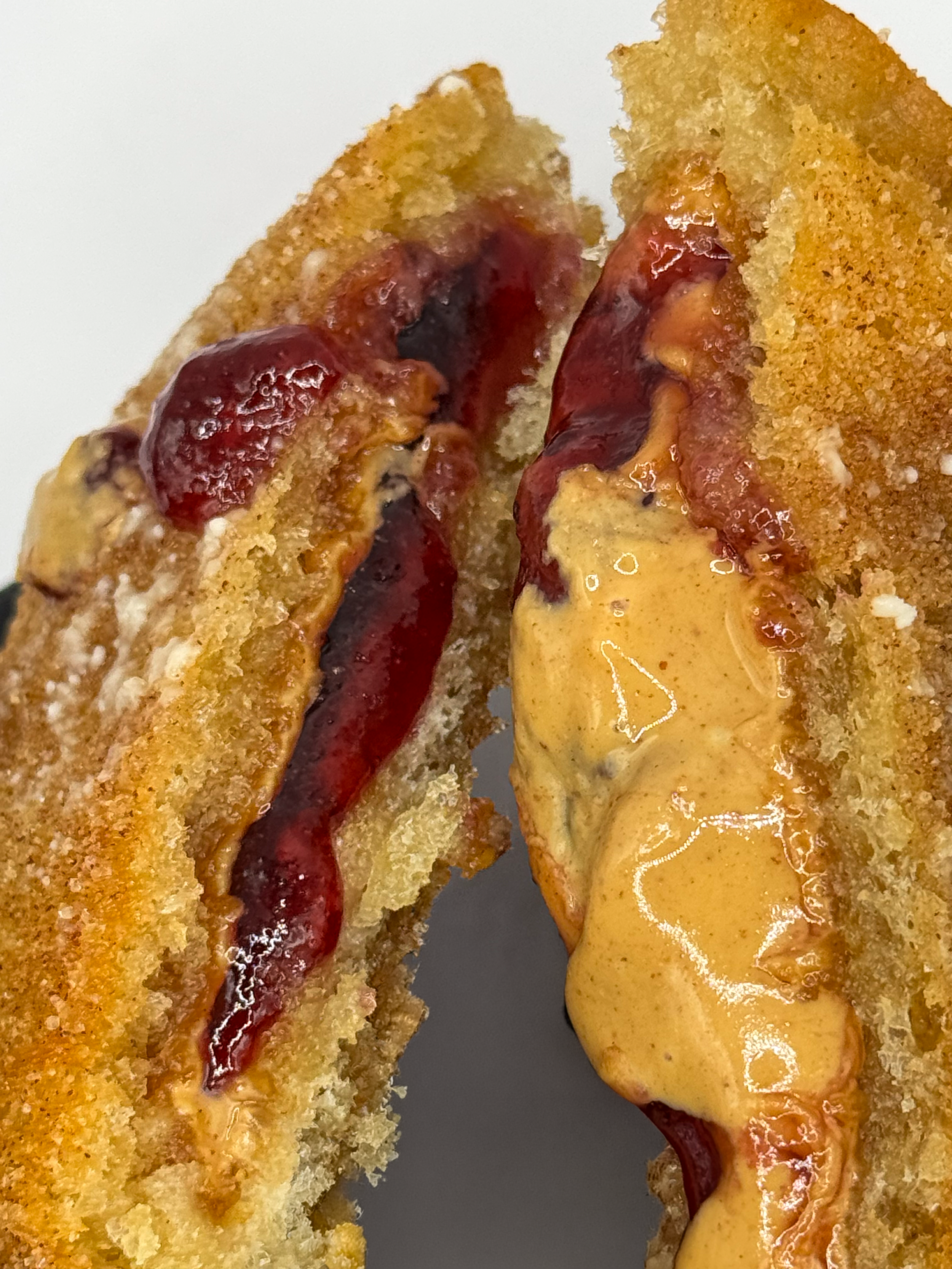 Close-up of a halved breaded fried sandwich filled with red jelly and creamy mustard.