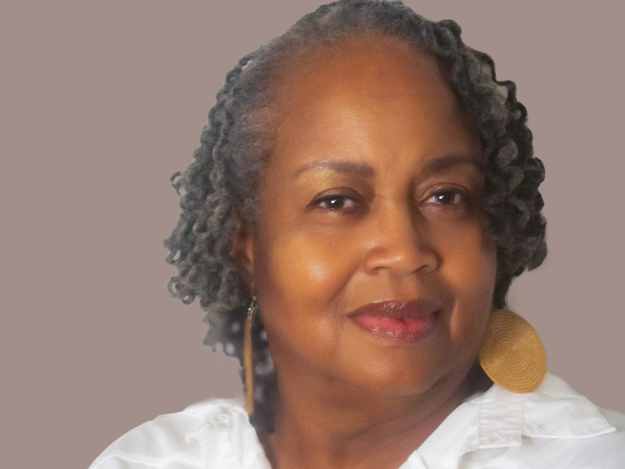 Close-up of author Yvette R Murray, a woman with short, curly gray hair, wearing a white blouse and large round gold earrings, smiling softly against a neutral background.