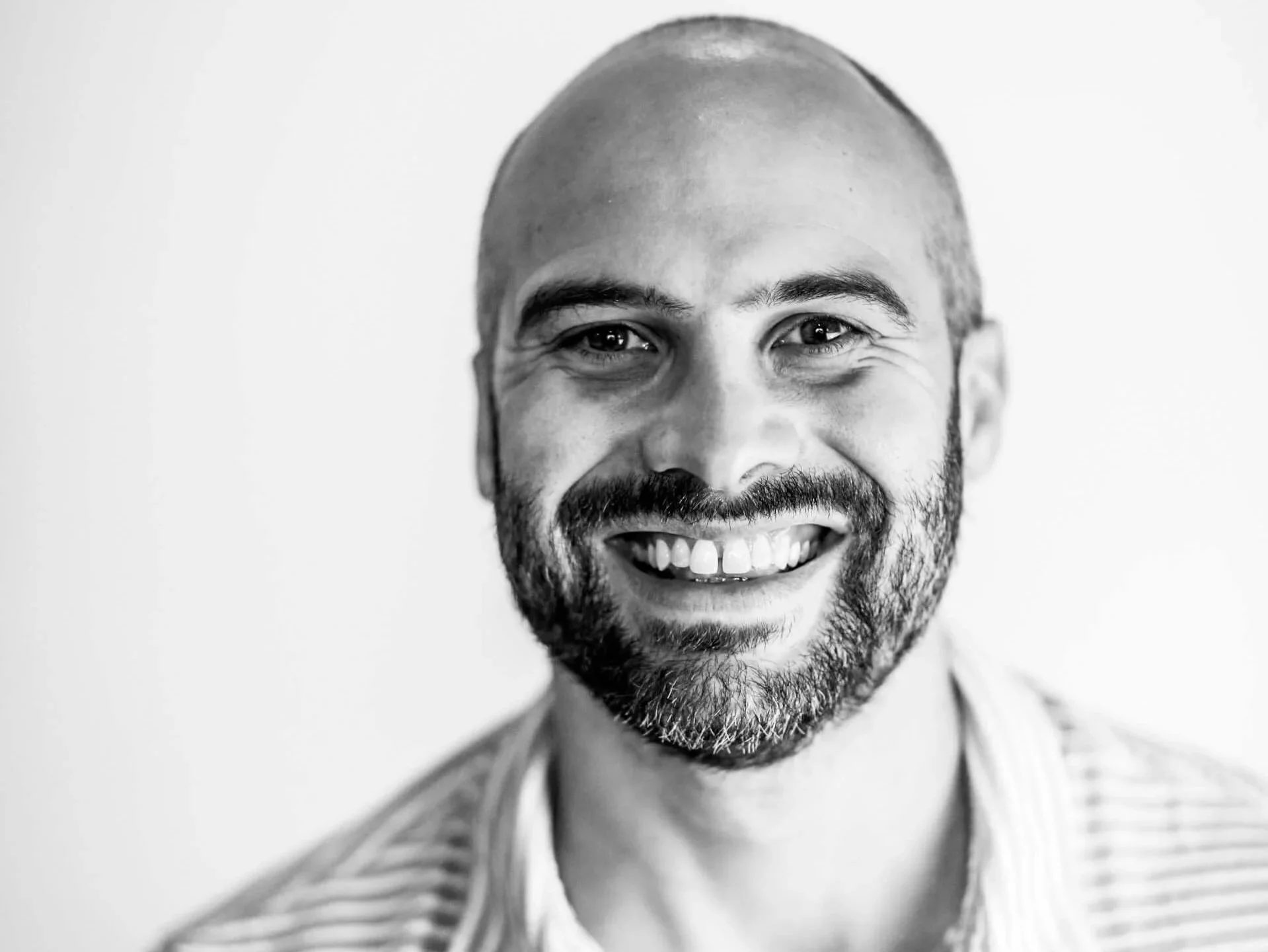 Black and white close-up portrait of author Brian Livingston, who is smiling, has a beard and short hair, and is wearing a striped shirt.