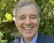 A smiling man, author Marvin Pontiff, with gray hair outdoors, with greenery in the background.