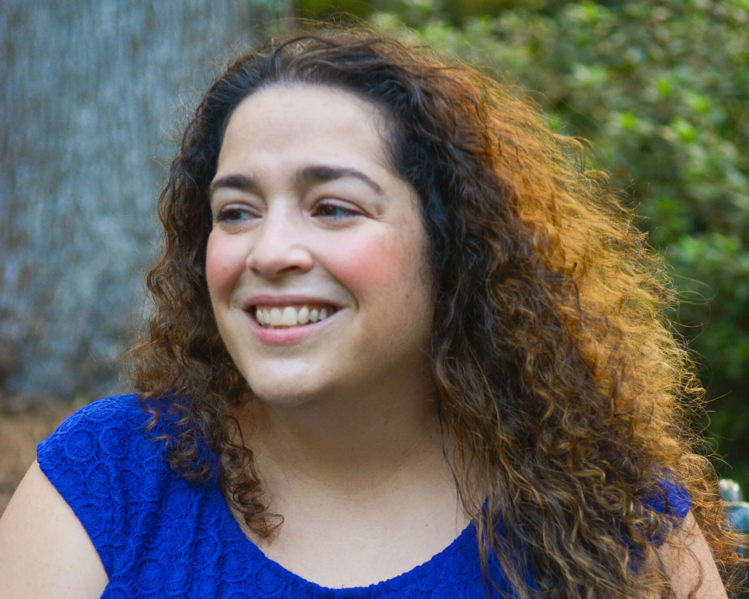 Author Elaine Reed, a woman with curly hair wearing a blue top outdoors, smiling and looking to her left.
