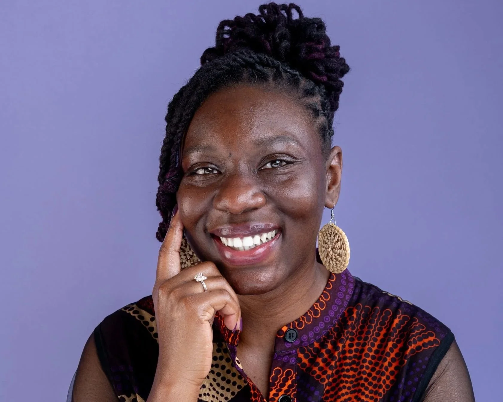 Author Ronda Taylor, a smiling woman with braided hair, wearing large woven earrings, a ring, and a colorful patterned top, against a purple background.