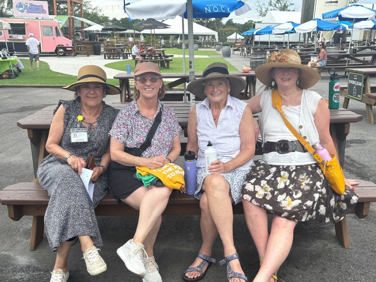 4 ladies wearing hats and smiling sitting on a bench