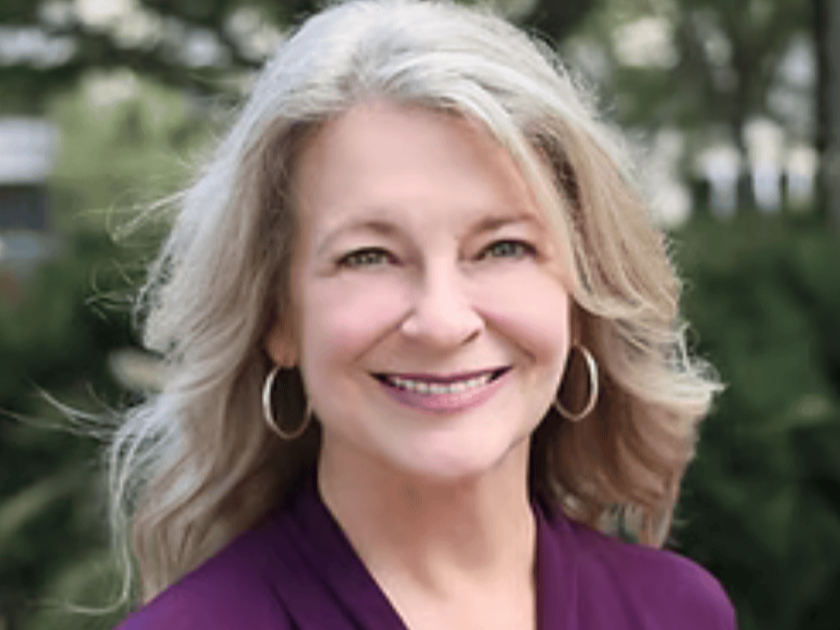 A smiling middle-aged woman, author Robin Hillyer-Miles, with blonde hair and hoop earrings outdoors.