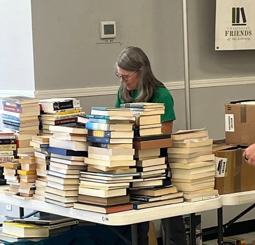 A woman sorting donated books with numerous stacks of books on a table in front of her.