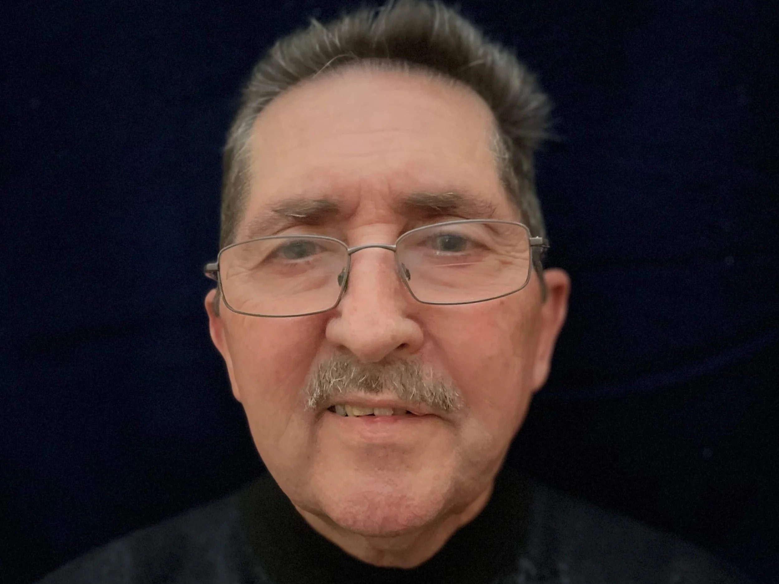 A close-up photo of a man, author Kenneth Kobularck with glasses, a mustache, and light-colored hair, smiling slightly against a dark background.