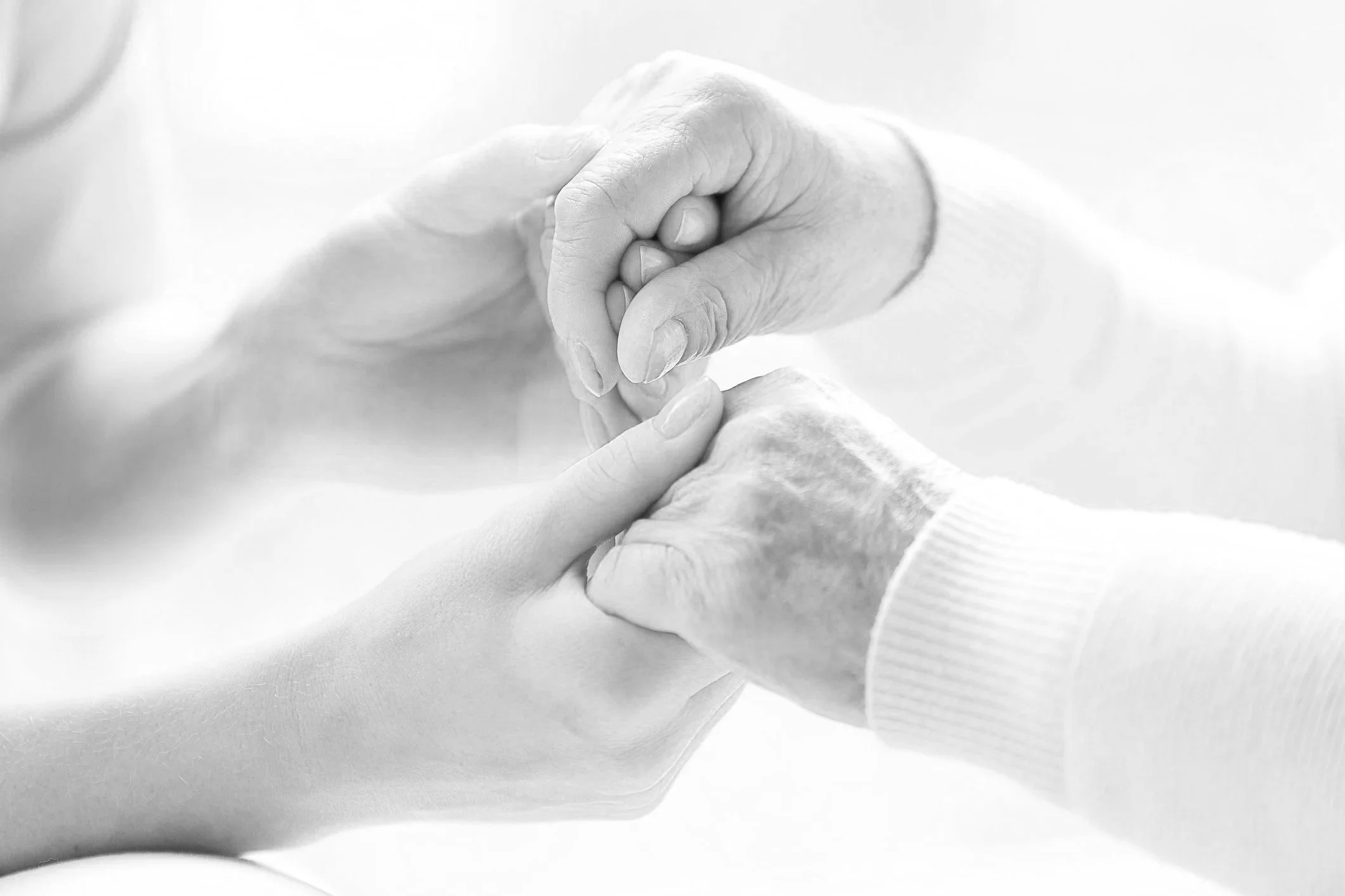Close-up of two hands gently holding each other, one appearing older and the other younger, symbolizing care and compassion.