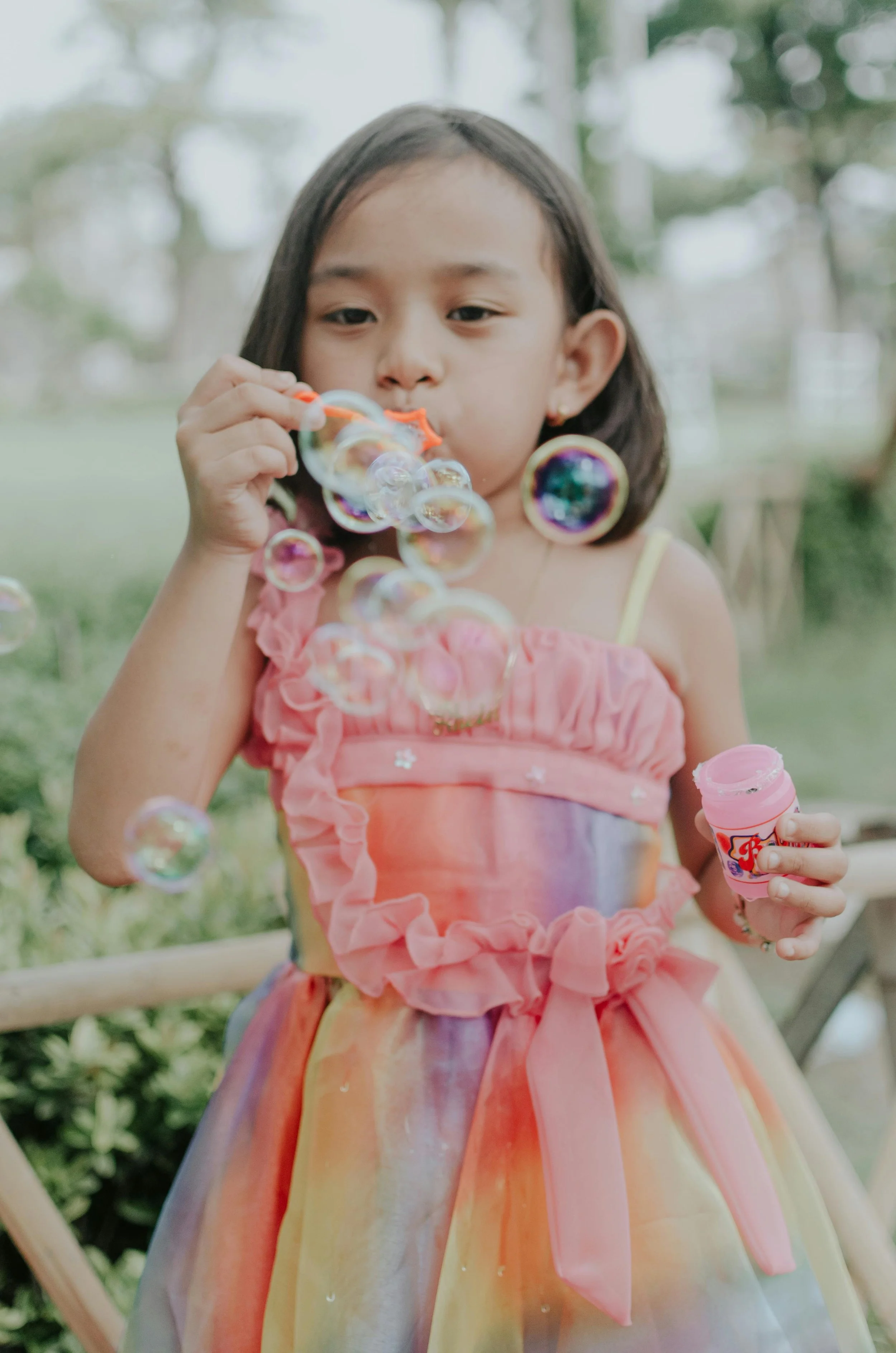 Young girl in a colorful dress blowing bubbles outdoors.