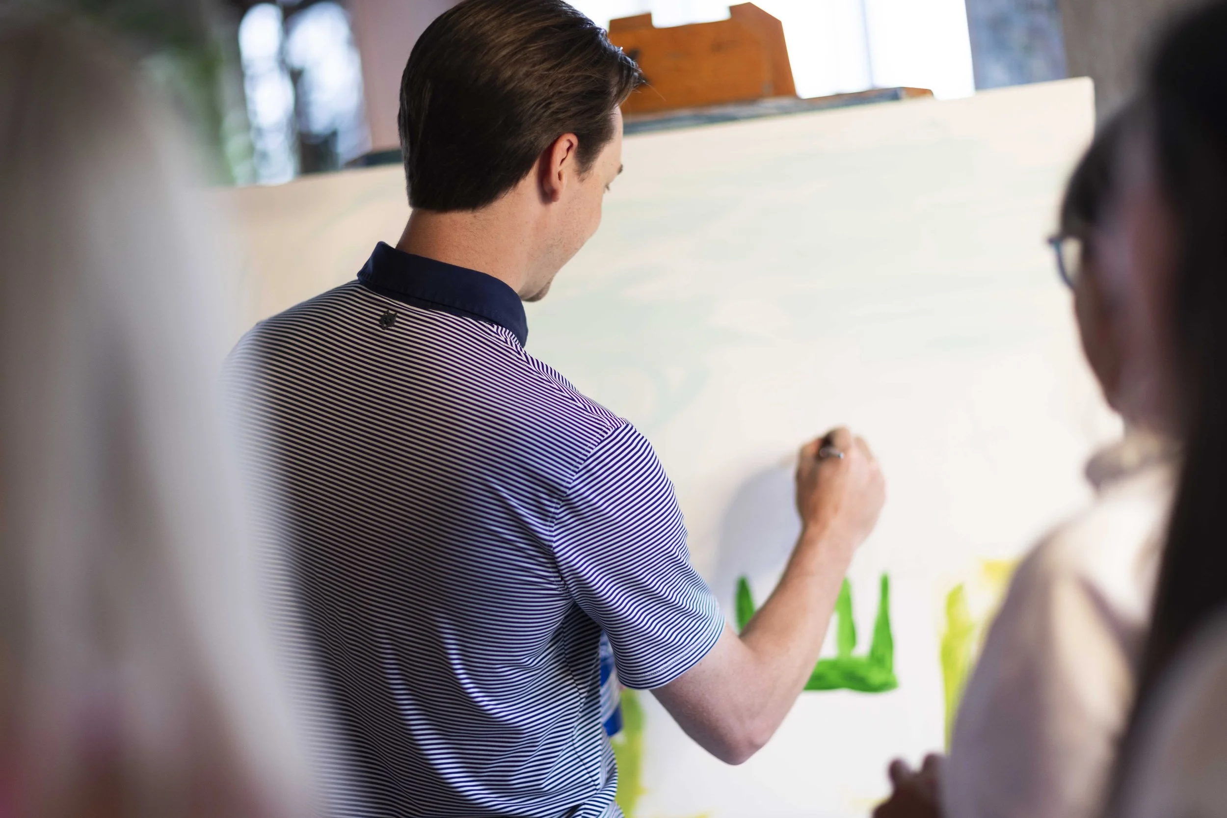 A man painting on a canvas, surrounded by people, at a private art event