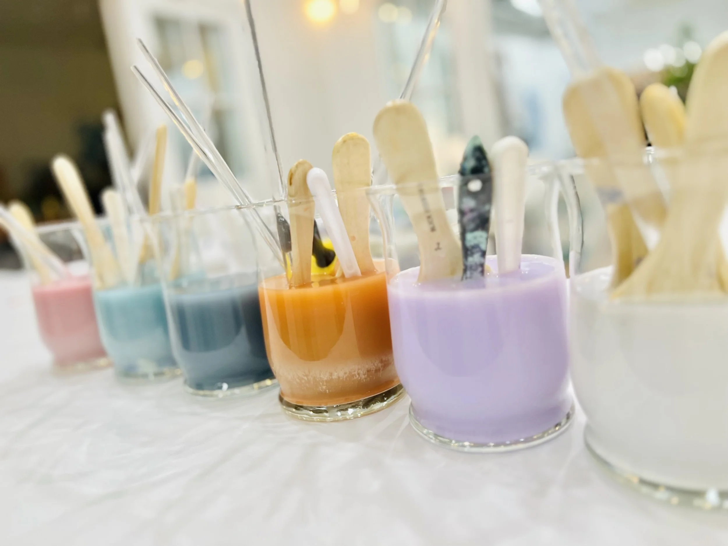 Jars filled with various colored paints and wooden sticks on a table.
