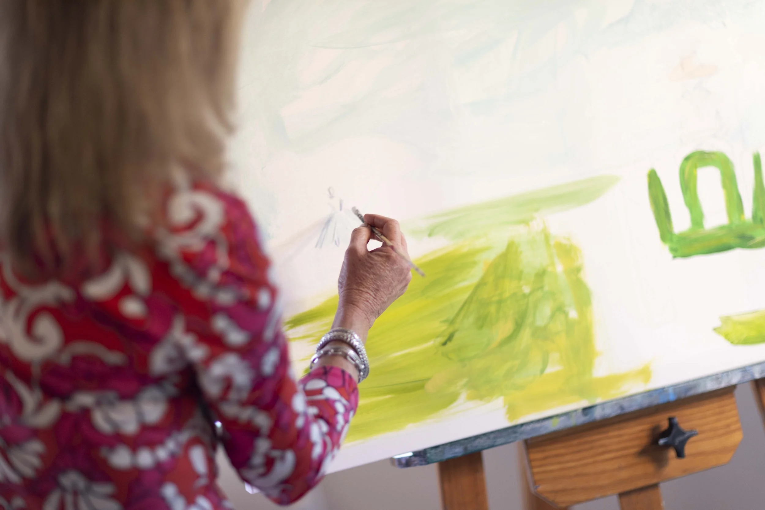 Person painting a landscape on a canvas with green and yellow colors.