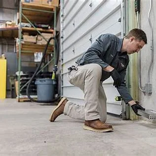 Man kneeling and working on a garage door in a garage