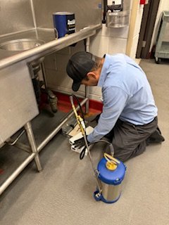 A pest control technician on the floor working in a commercial kitchen.