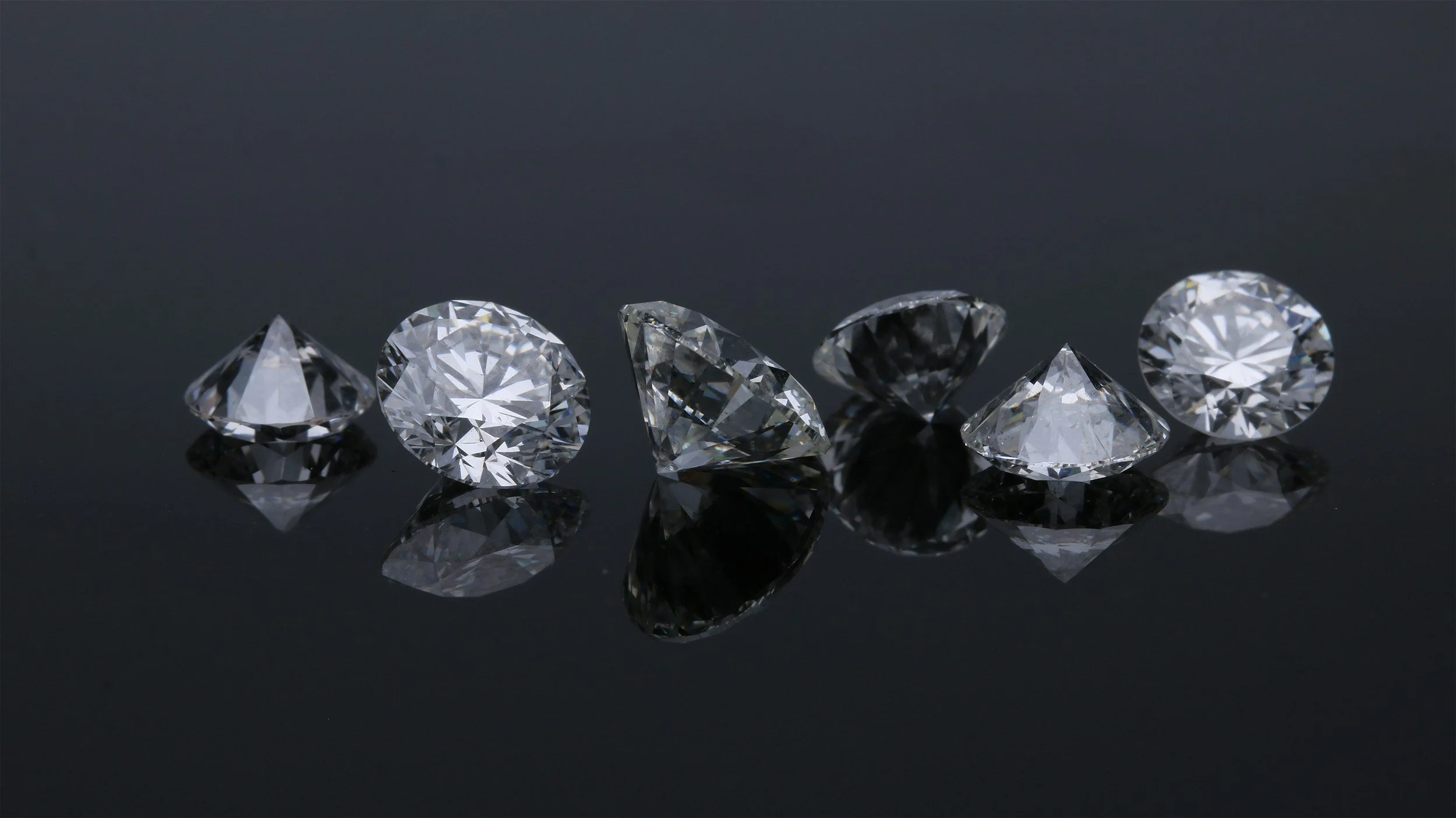Six loose diamonds arranged on a black reflective surface.