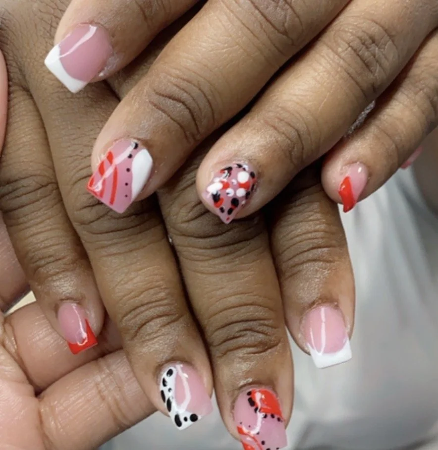 Close-up of a person's hands showing nails with pink nail polish and various colorful abstract patterns in red, black, and white.