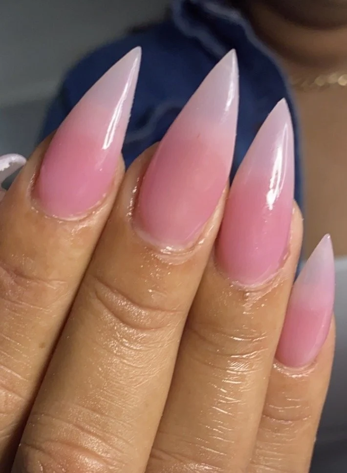 Close-up of manicured nails painted in a pink ombre design, with sharp stiletto shape.