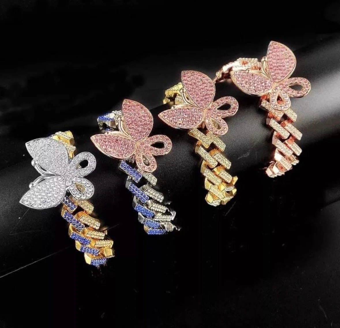 Three butterfly-shaped bracelets with sparkling stones in gold, silver, and rose gold colors, displayed on a black surface.