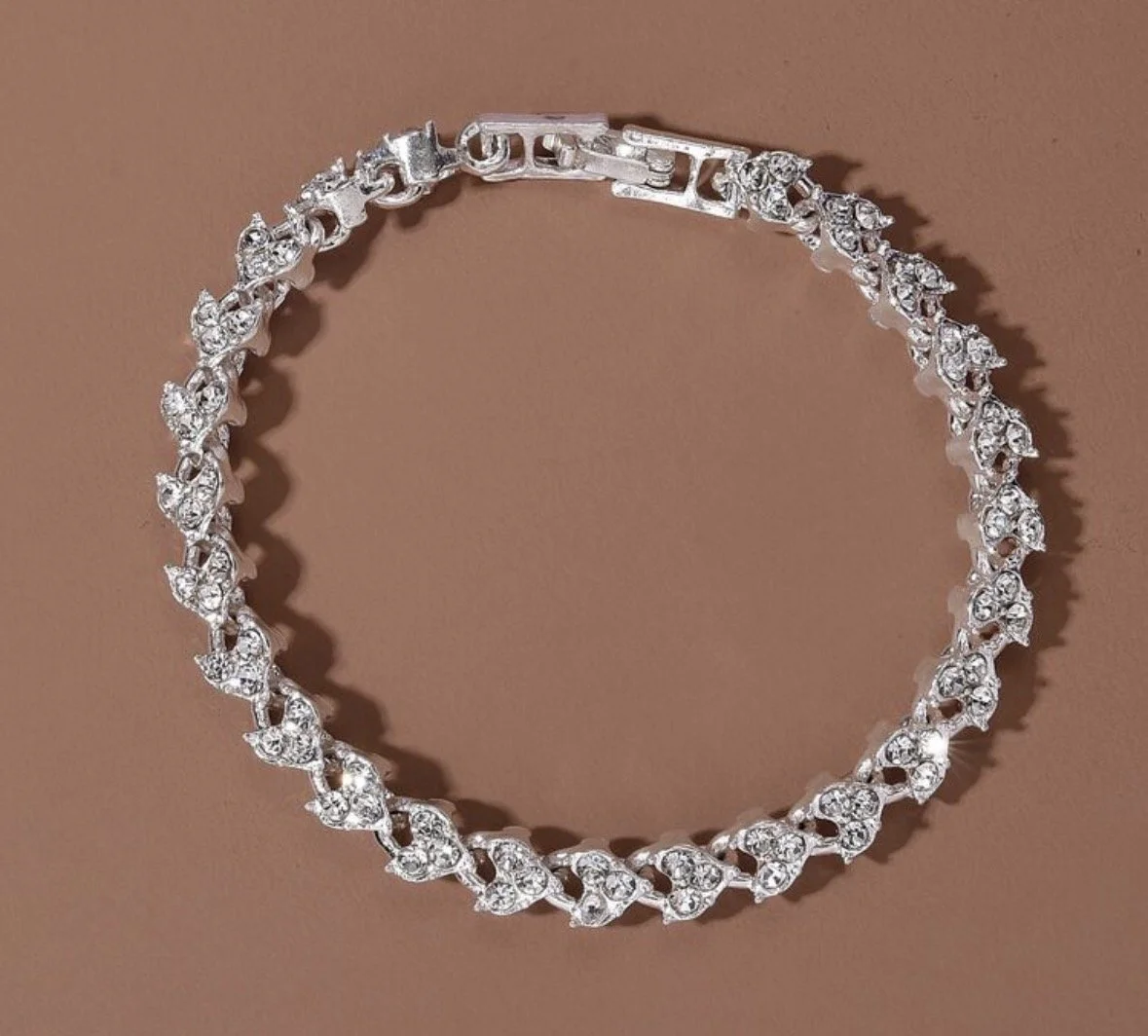 A silver bracelet adorned with multiple small, sparkling diamonds arranged in a floral pattern, laid on a neutral colored surface.